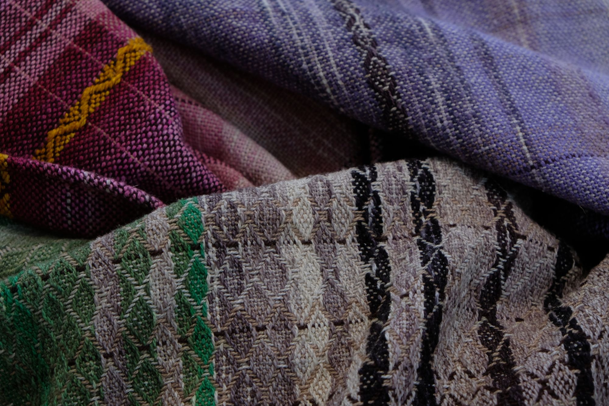 handwoven, hand dyed fabric of many colors with a diamond pattern, folded on a wooden floor.