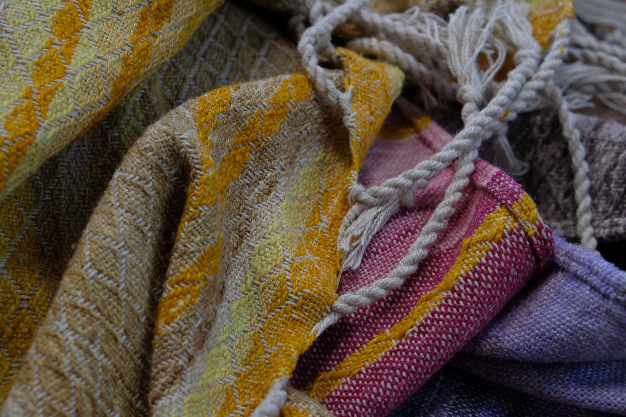 handwoven, hand dyed fabric of many colors with a diamond pattern, folded on a wooden floor.