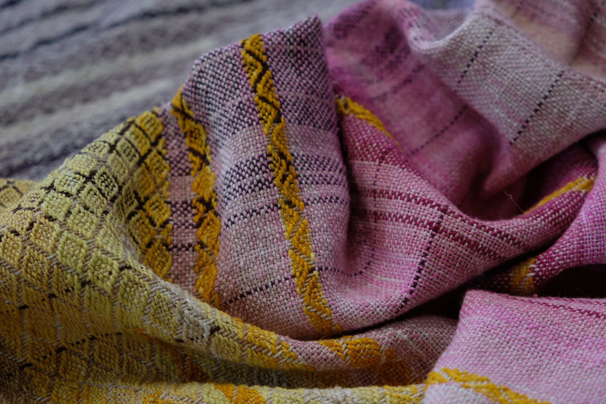 handwoven, hand dyed fabric of many colors with a diamond pattern, laid out on a wooden floor.