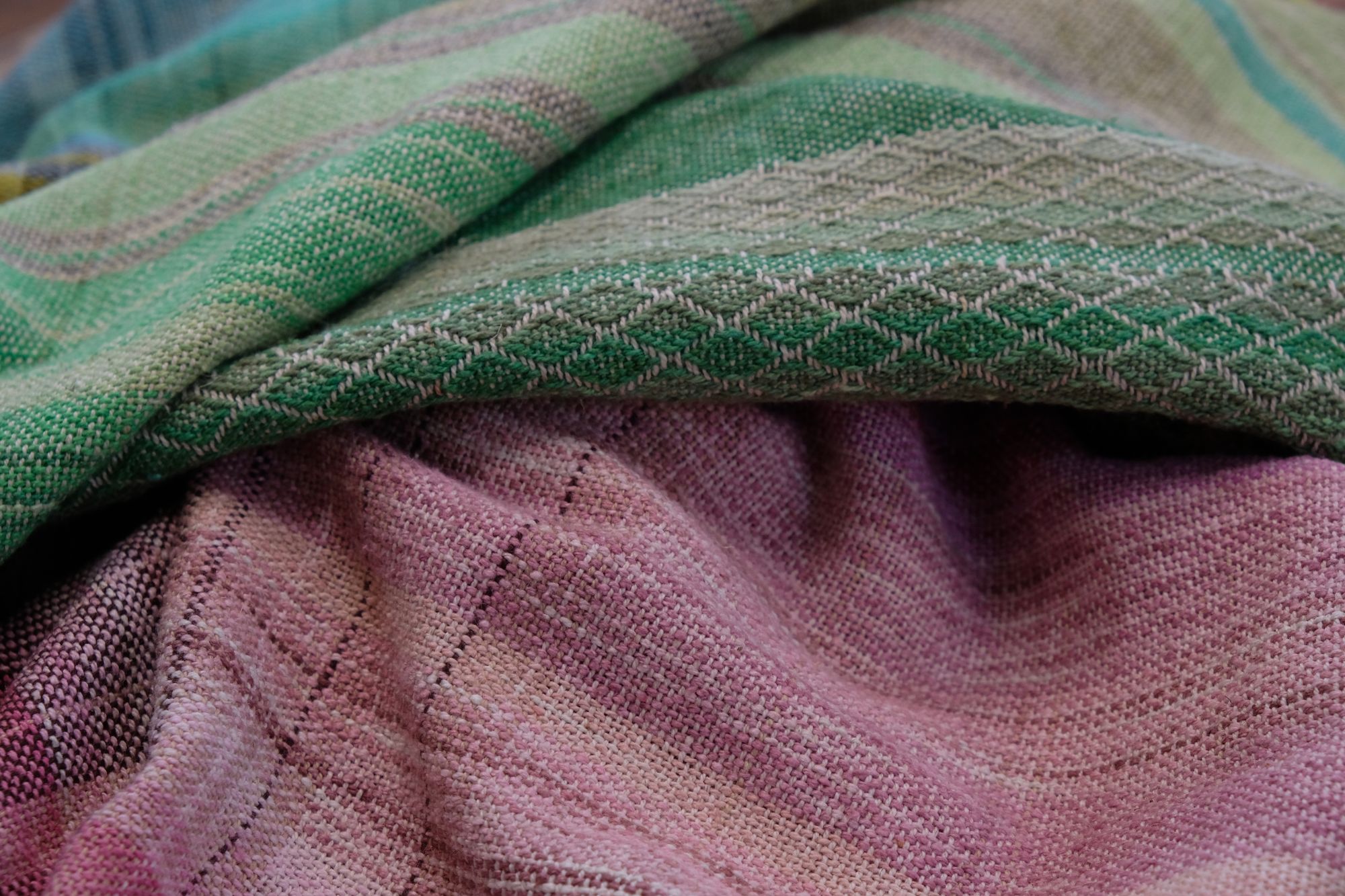 handwoven, hand dyed fabric of many colors with a diamond pattern, laid out on a wooden floor.