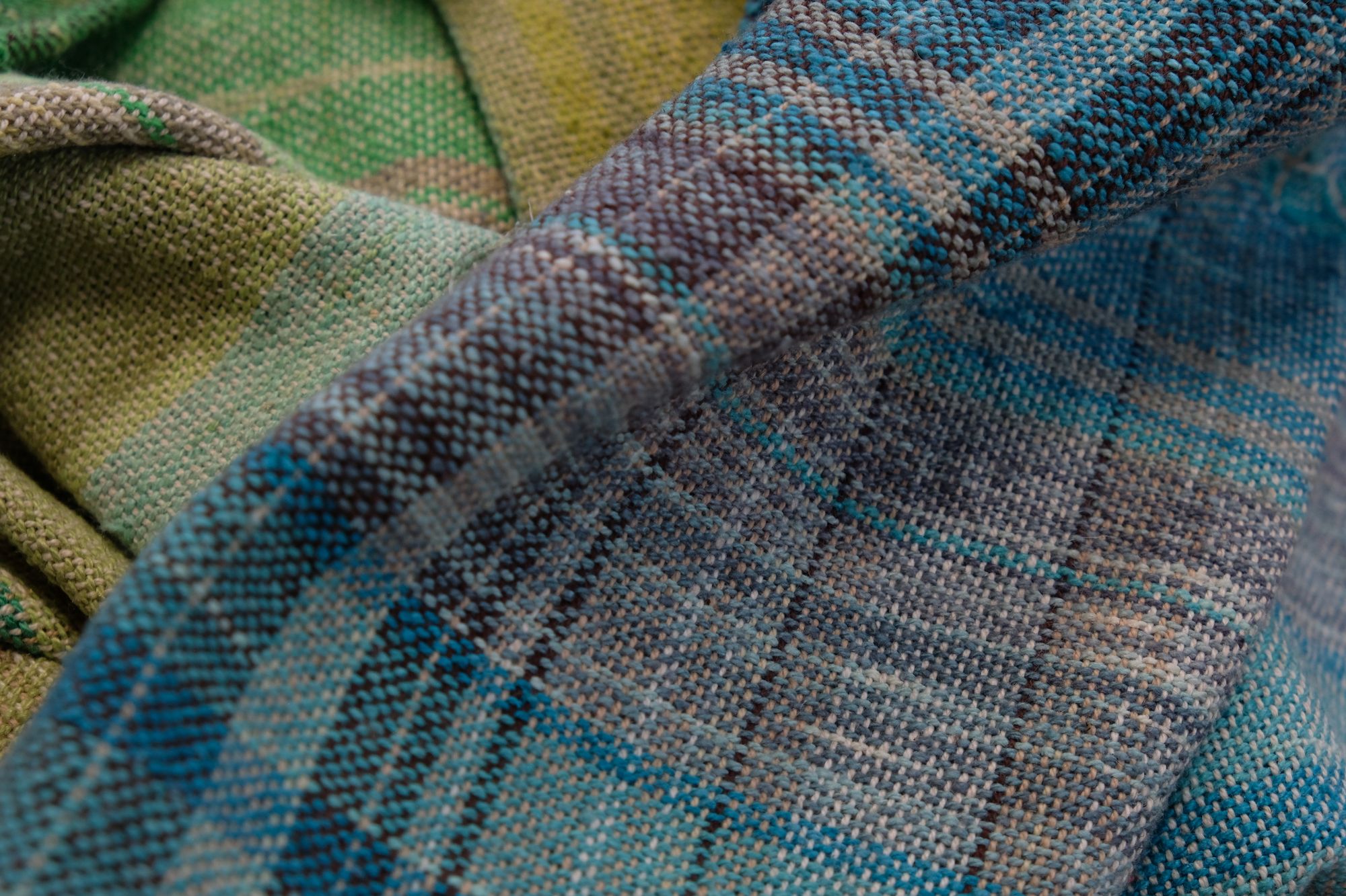 handwoven, hand dyed fabric of many colors with a diamond pattern, folded on a wooden floor.