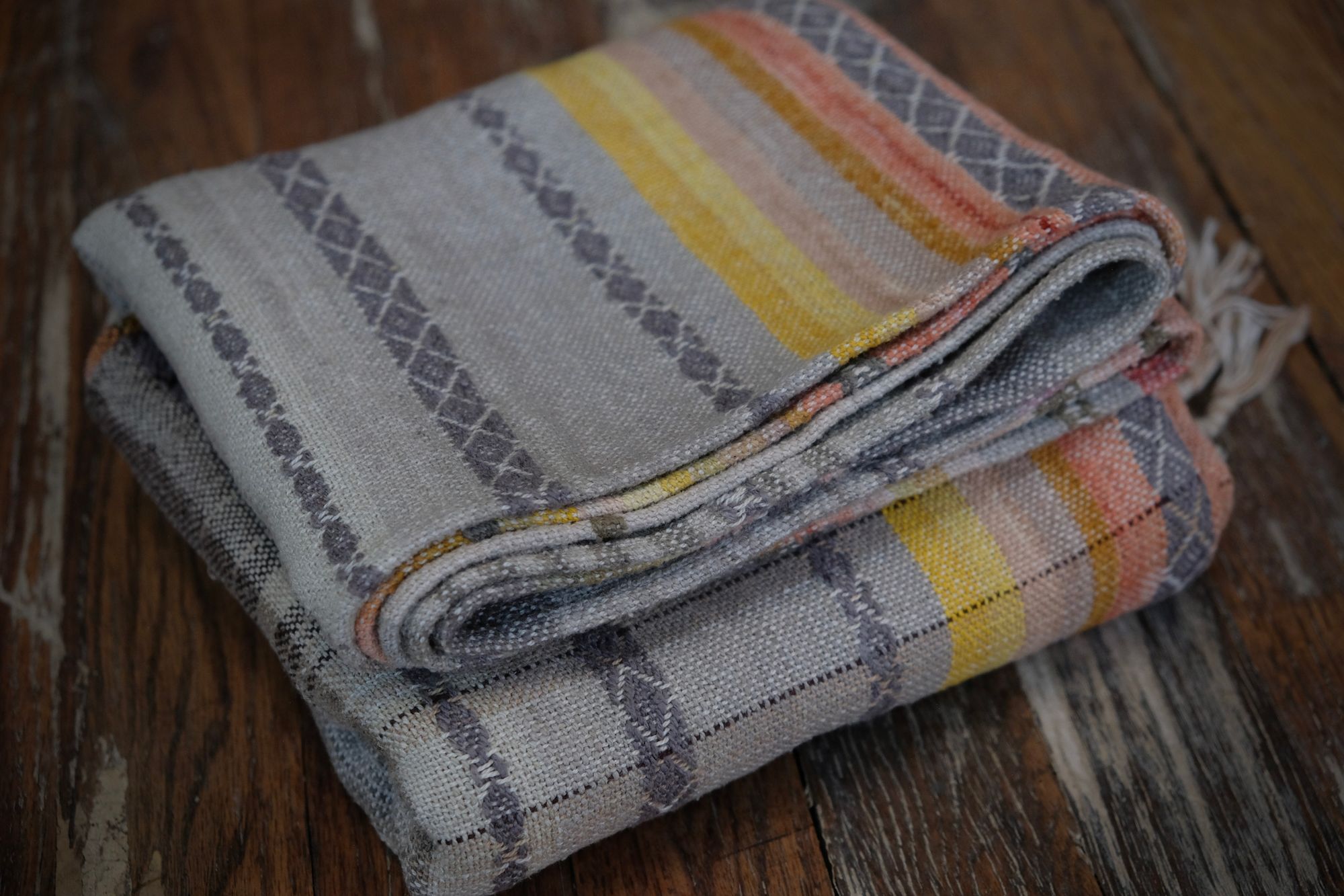 Details of a handwoven shawl in soft but brilliant naturally dyed shades of gray, yellow, pink, salmon, orange, green and purple. The shawl is designed with small stripes of all these colors, and pattern-texture woven details, also of tiny stripes