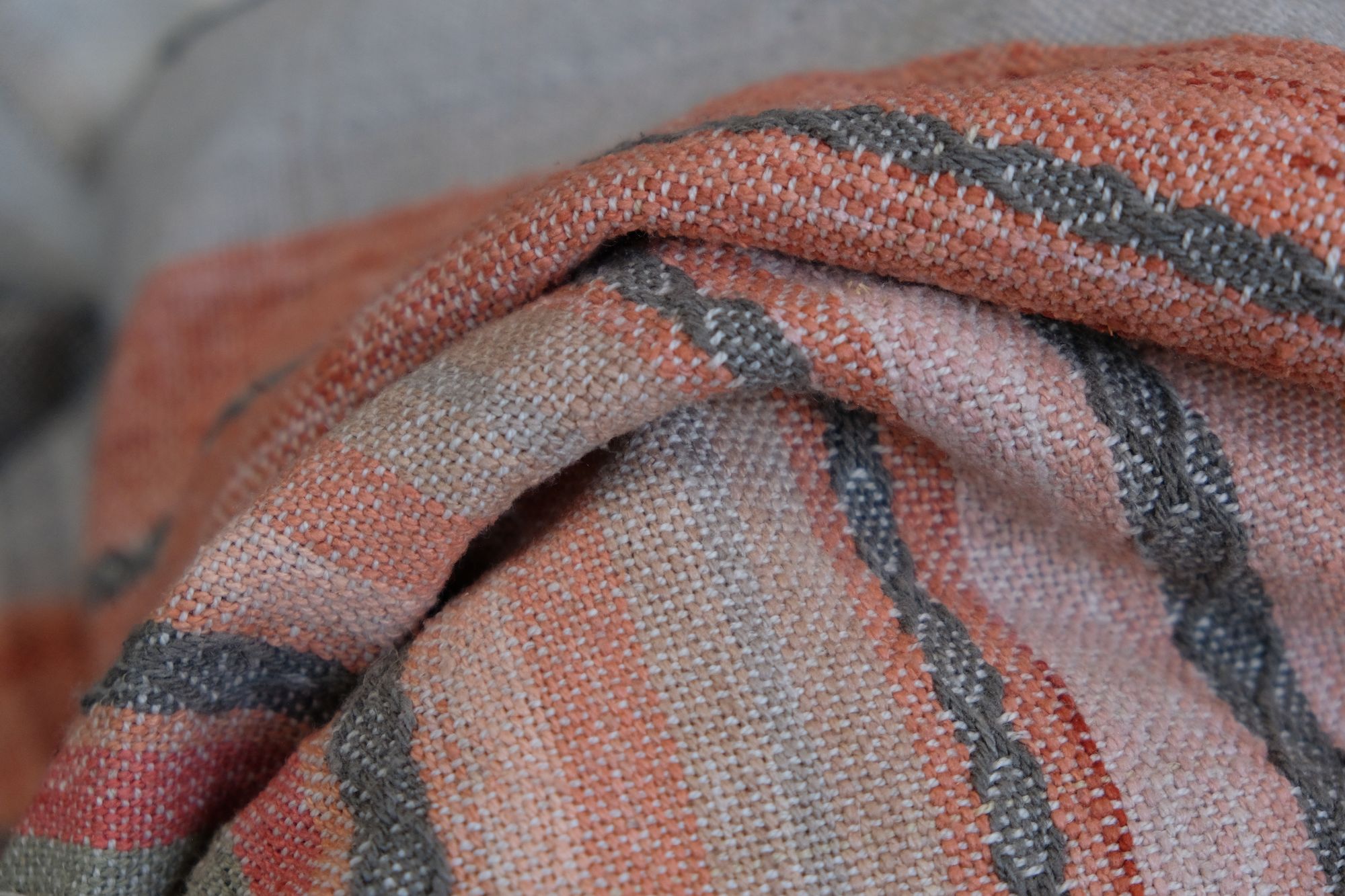 Details of a handwoven shawl in soft but brilliant naturally dyed shades of gray, yellow, pink, salmon, orange, green and purple. The shawl is designed with small stripes of all these colors, and pattern-texture woven details, also of tiny stripes