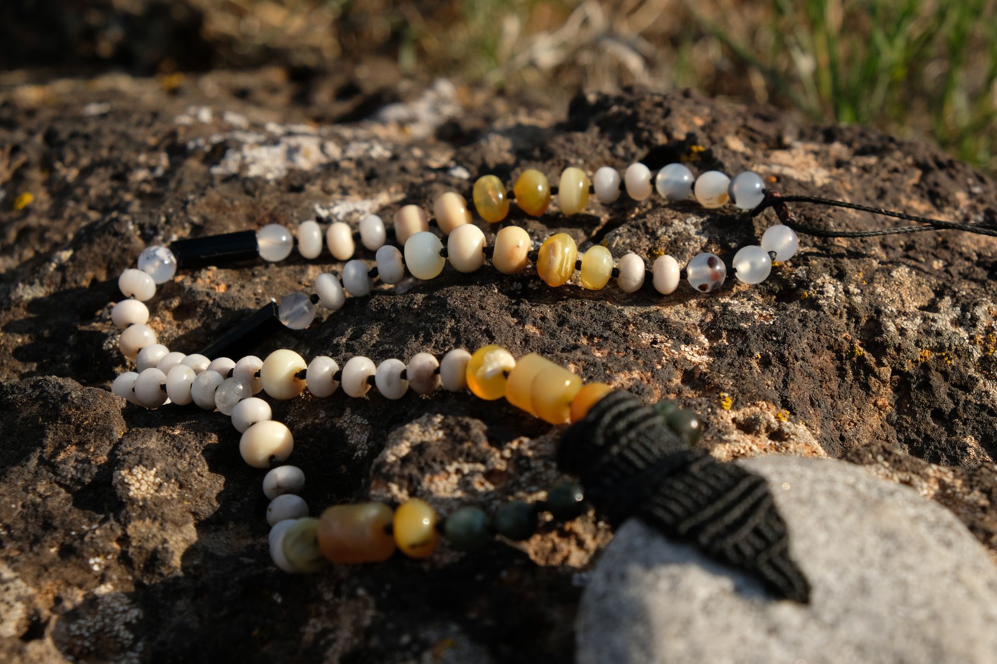 A necklace of green, white, opal and black semi-precious stones, with a moon-shaped gray granite stone, adorned with a basket, rests on a lichen covered rock in New Mexico at sunset