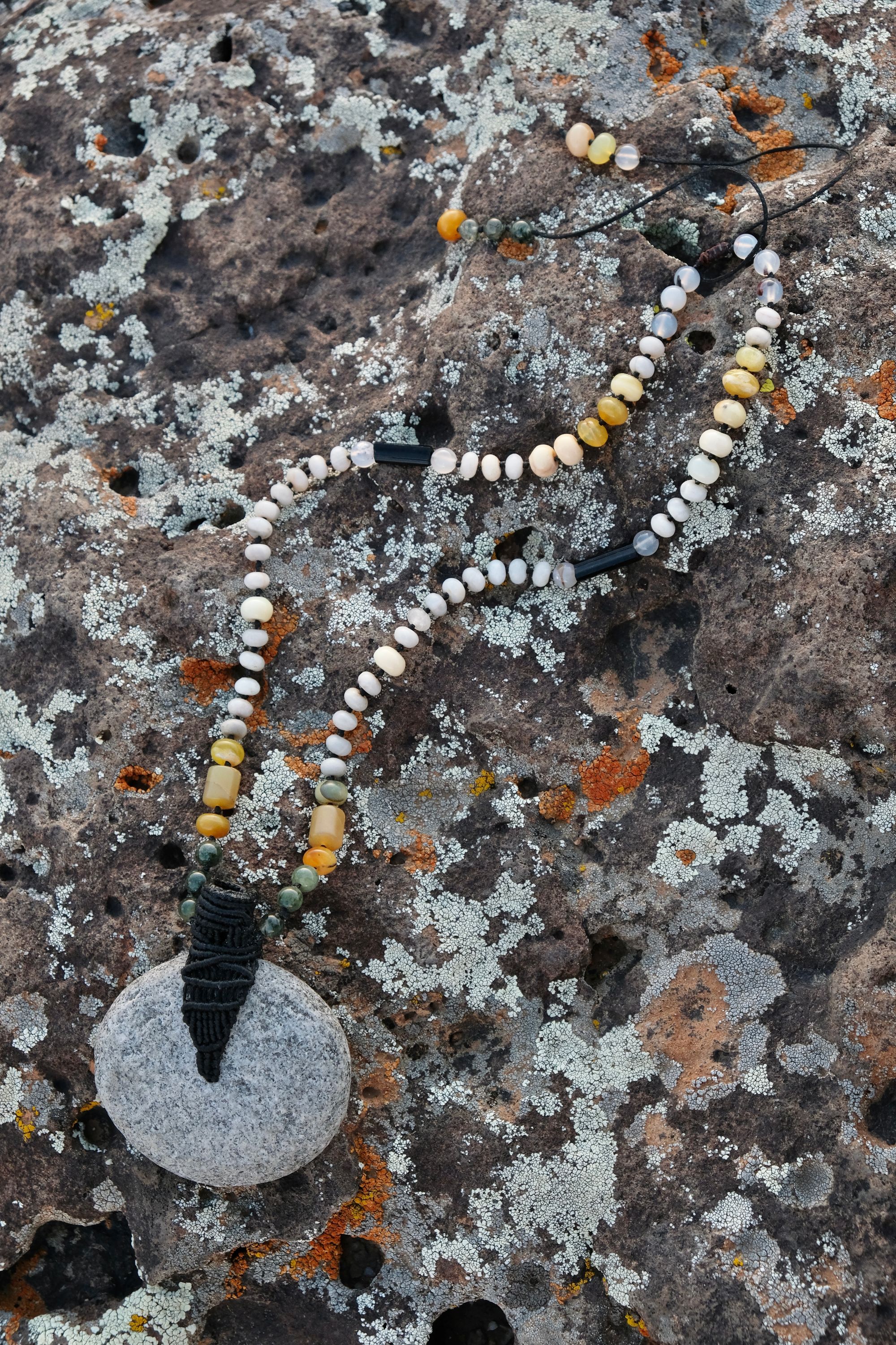A necklace of green, white, opal and black semi-precious stones, with a moon-shaped gray granite stone, adorned with a basket, rests on a lichen covered rock in New Mexico at sunset