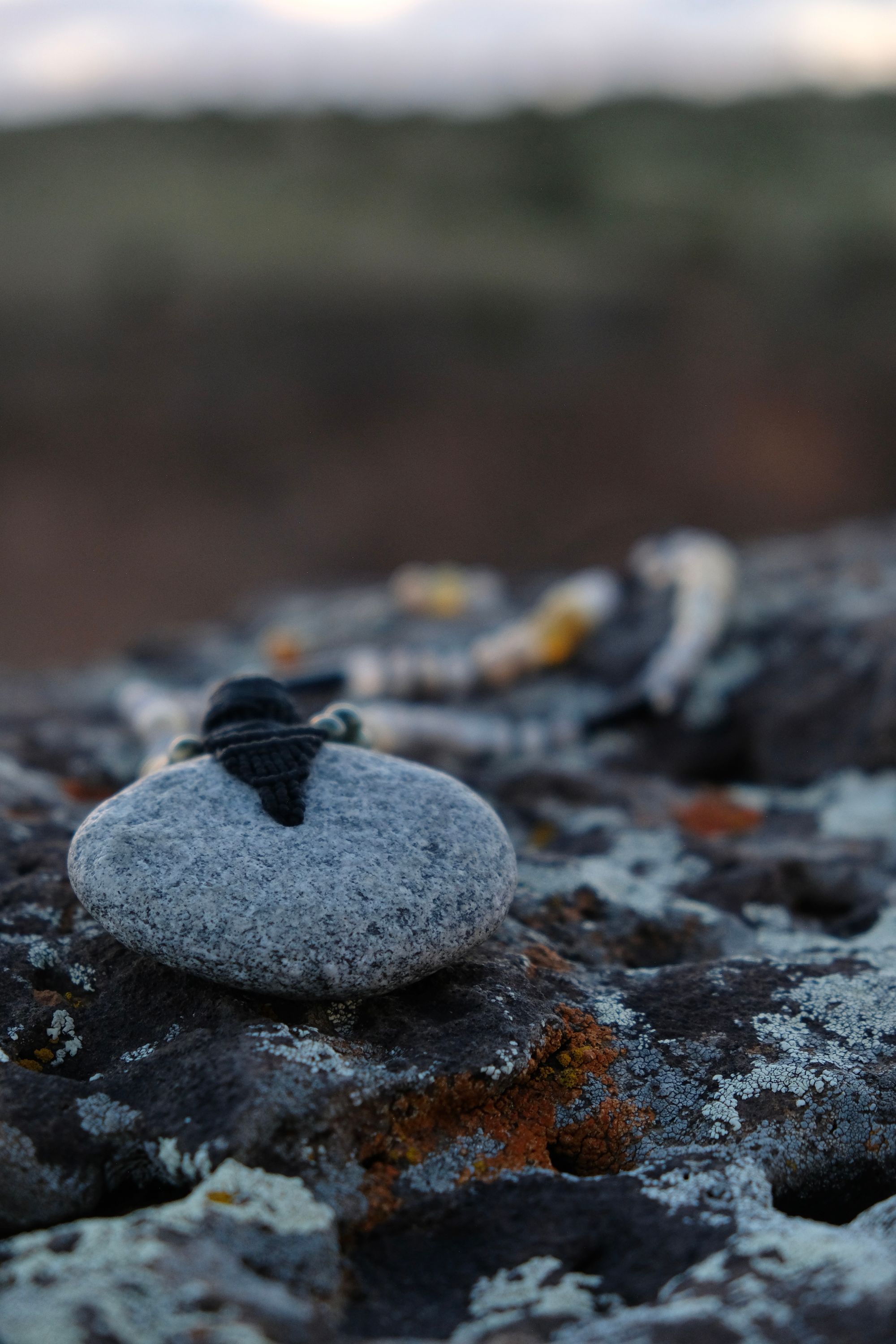 A necklace of green, white, opal and black semi-precious stones, with a moon-shaped gray granite stone, adorned with a basket, rests on a lichen covered rock in New Mexico at sunset