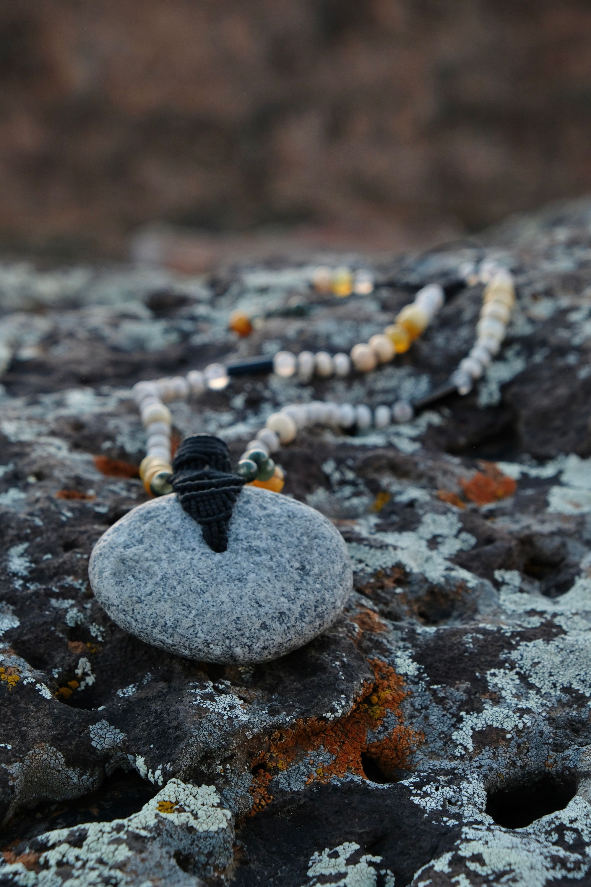 A necklace of green, white, opal and black semi-precious stones, with a moon-shaped gray granite stone, adorned with a basket, rests on a lichen covered rock in New Mexico at sunset