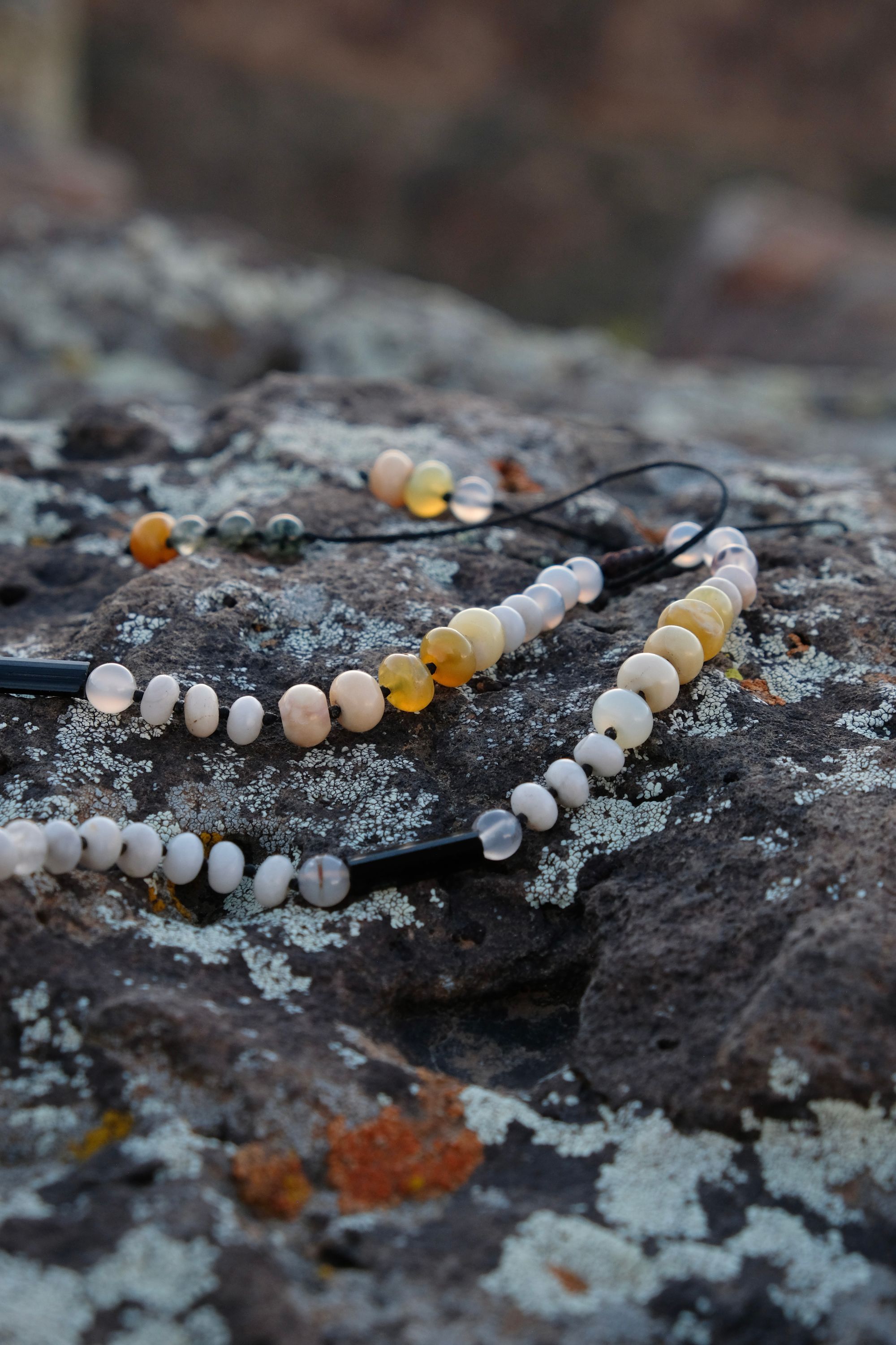 A necklace of green, white, opal and black semi-precious stones, with a moon-shaped gray granite stone, adorned with a basket, rests on a lichen covered rock in New Mexico at sunset