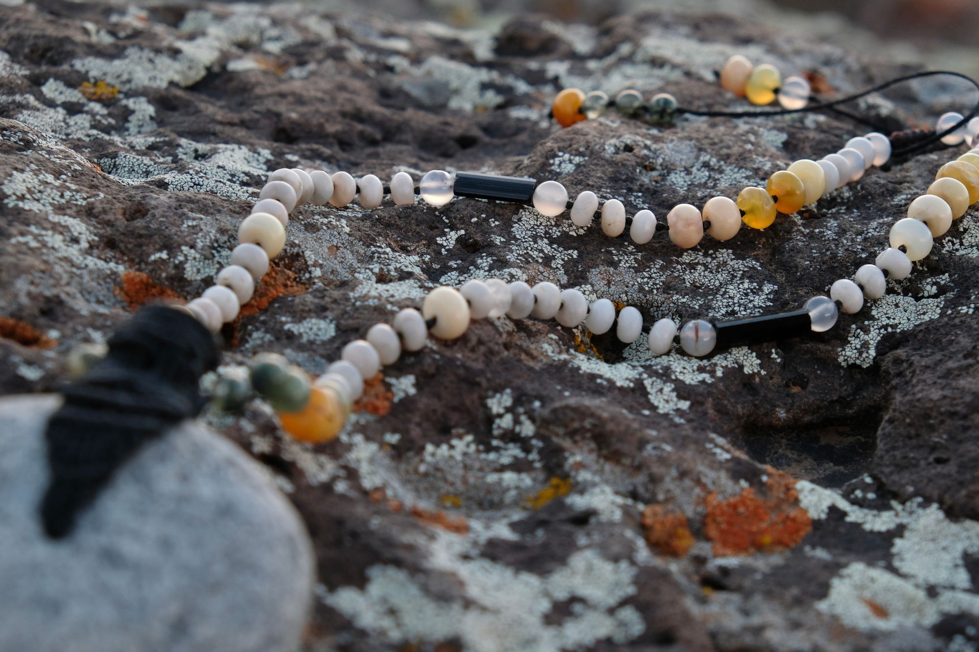 A necklace of green, white, opal and black semi-precious stones, with a moon-shaped gray granite stone, adorned with a basket, rests on a lichen covered rock in New Mexico at sunset