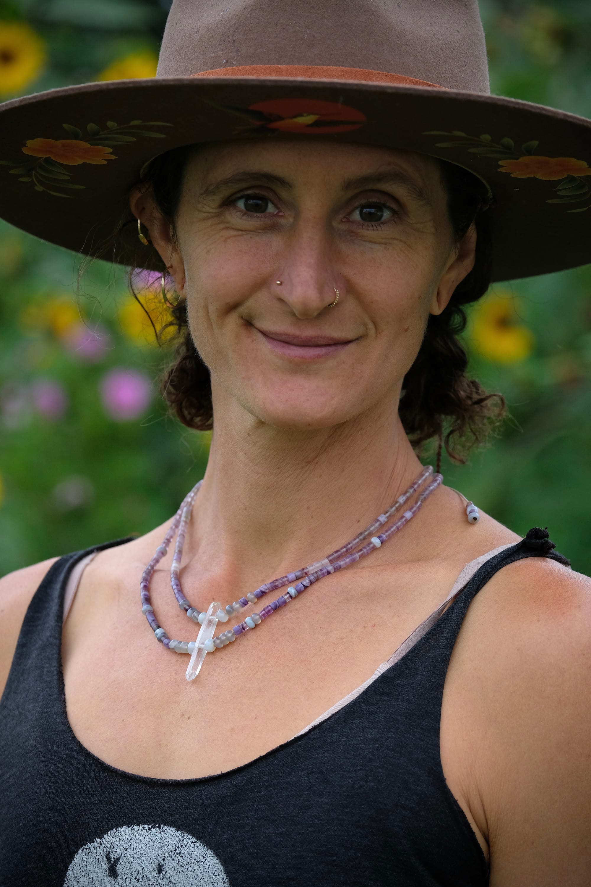 A woman wears a beaded necklace made of purple fluorite, gray quartz and a clear quartz crystal 