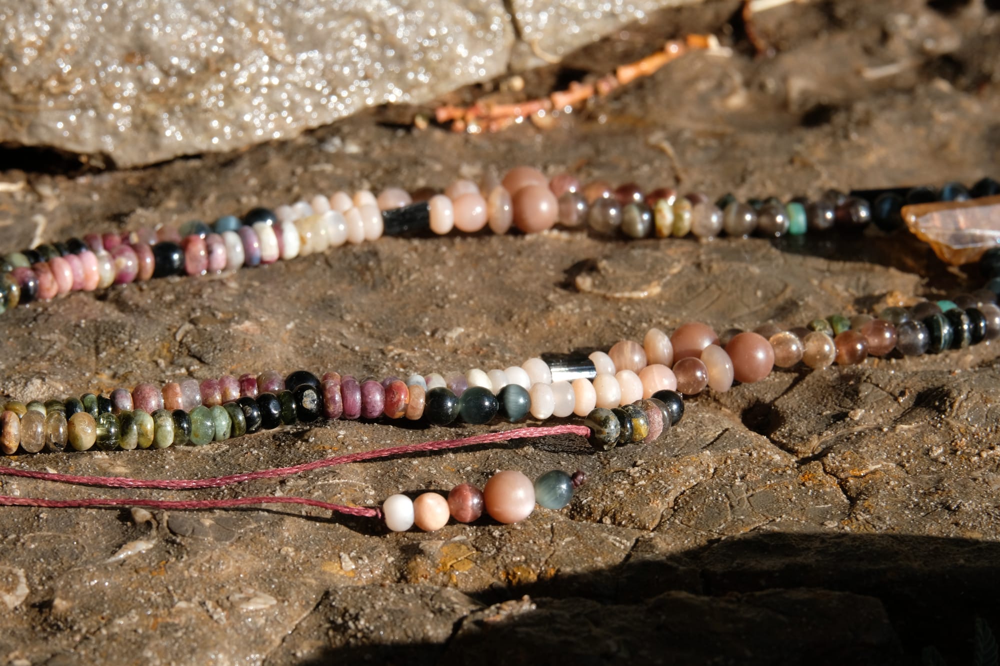 A citrine, cat's eye, tourmaline and emerald necklace by Jeannie Ortiza necklace of luminous semi precious stones in golden citrine, black, dusty pink and deep green rests on a stone embedded with fossils