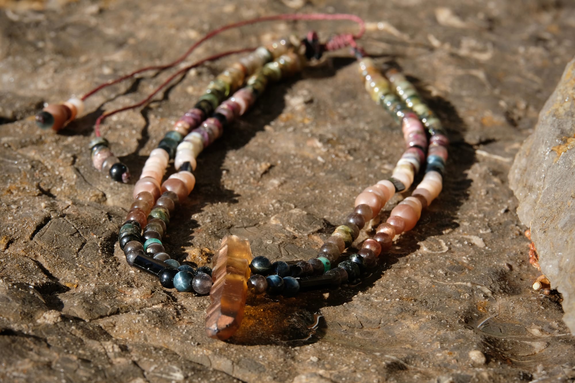 A citrine, cat's eye, tourmaline and emerald necklace by Jeannie Ortiza necklace of luminous semi precious stones in golden citrine, black, dusty pink and deep green rests on a stone embedded with fossils