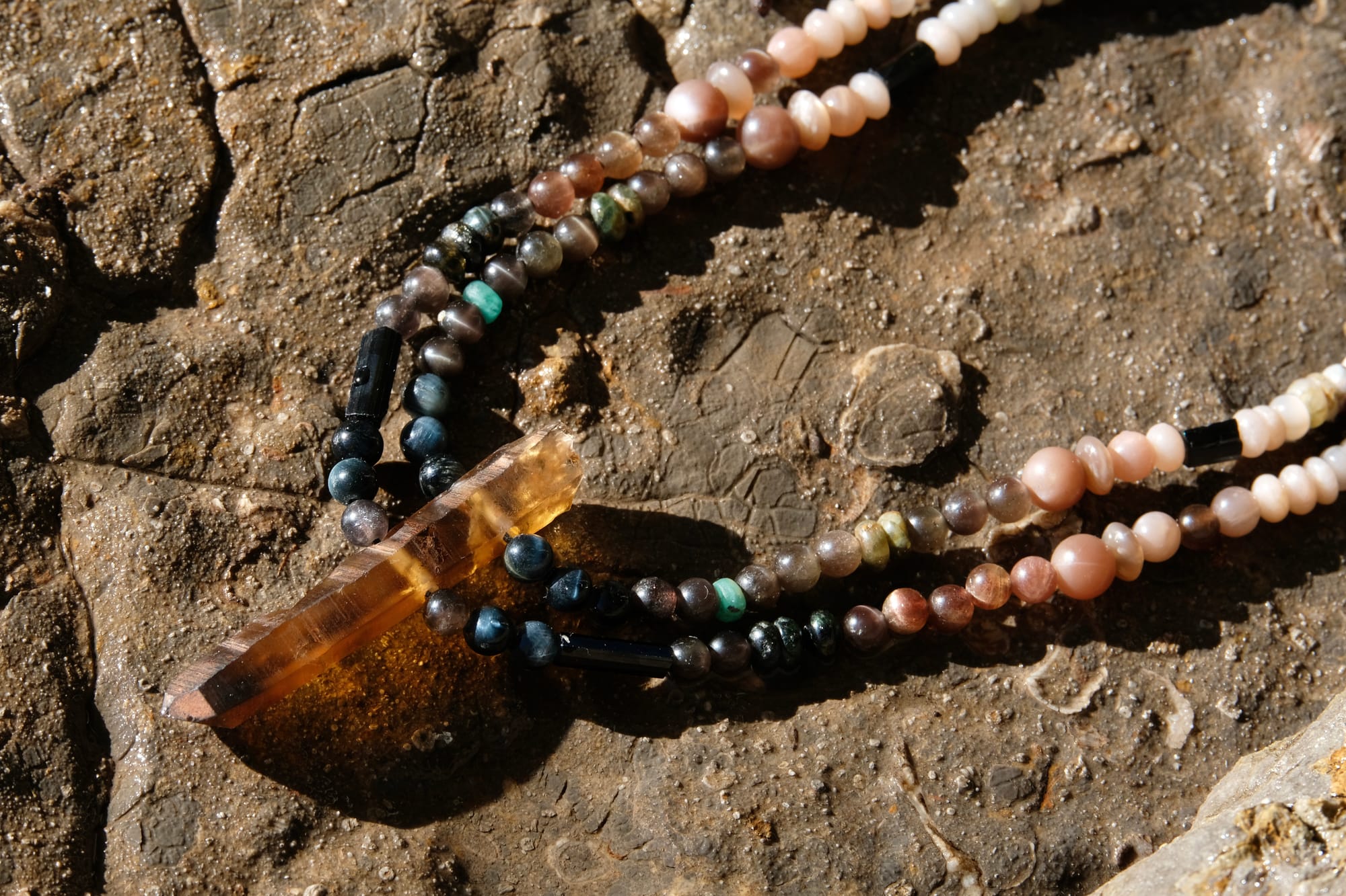 A citrine, cat's eye, tourmaline and emerald necklace by Jeannie Ortiza necklace of luminous semi precious stones in golden citrine, black, dusty pink and deep green rests on a stone embedded with fossils