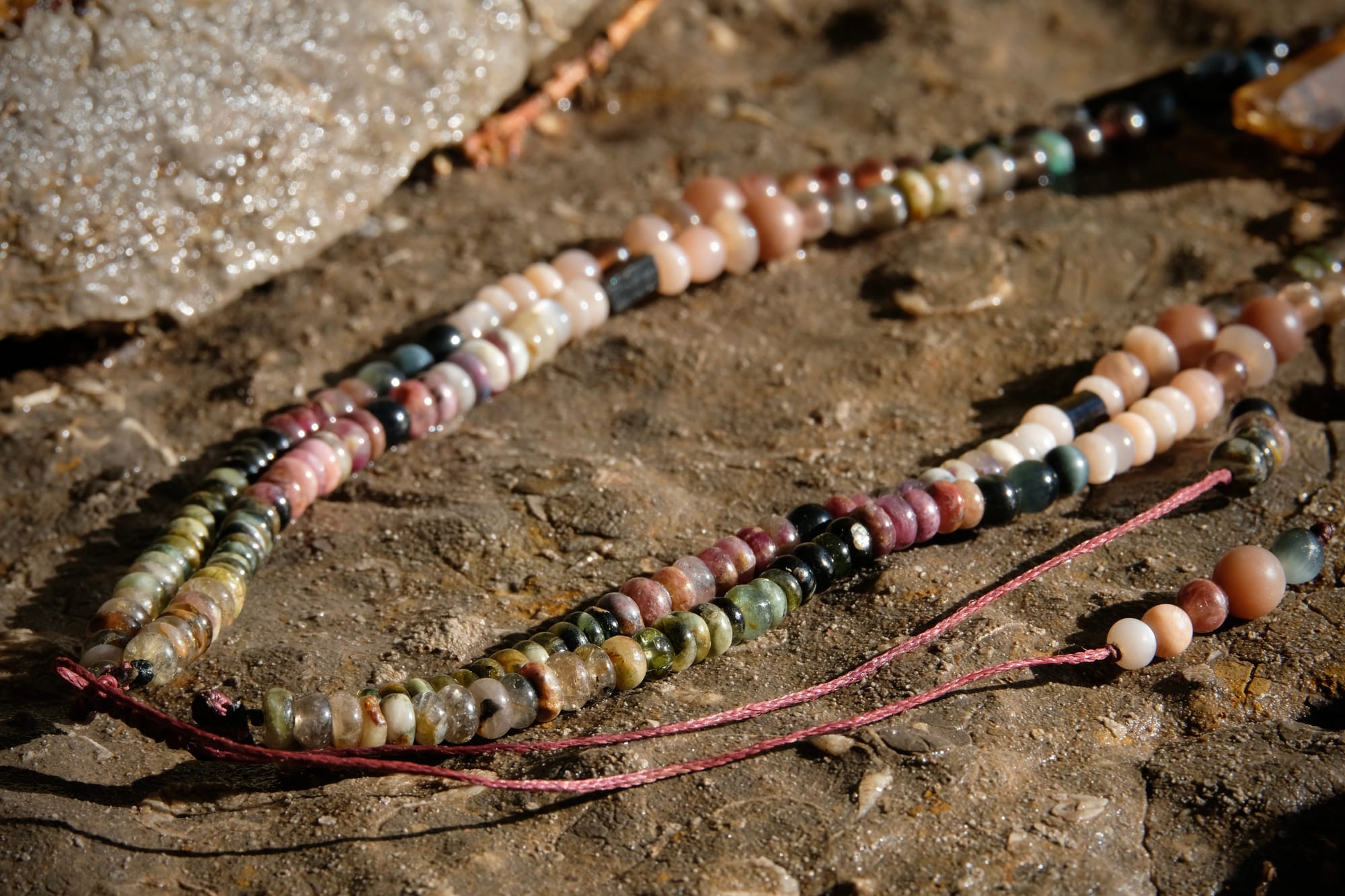 A citrine, cat's eye, tourmaline and emerald necklace by Jeannie Ortiza necklace of luminous semi precious stones in golden citrine, black, dusty pink and deep green rests on a stone embedded with fossils