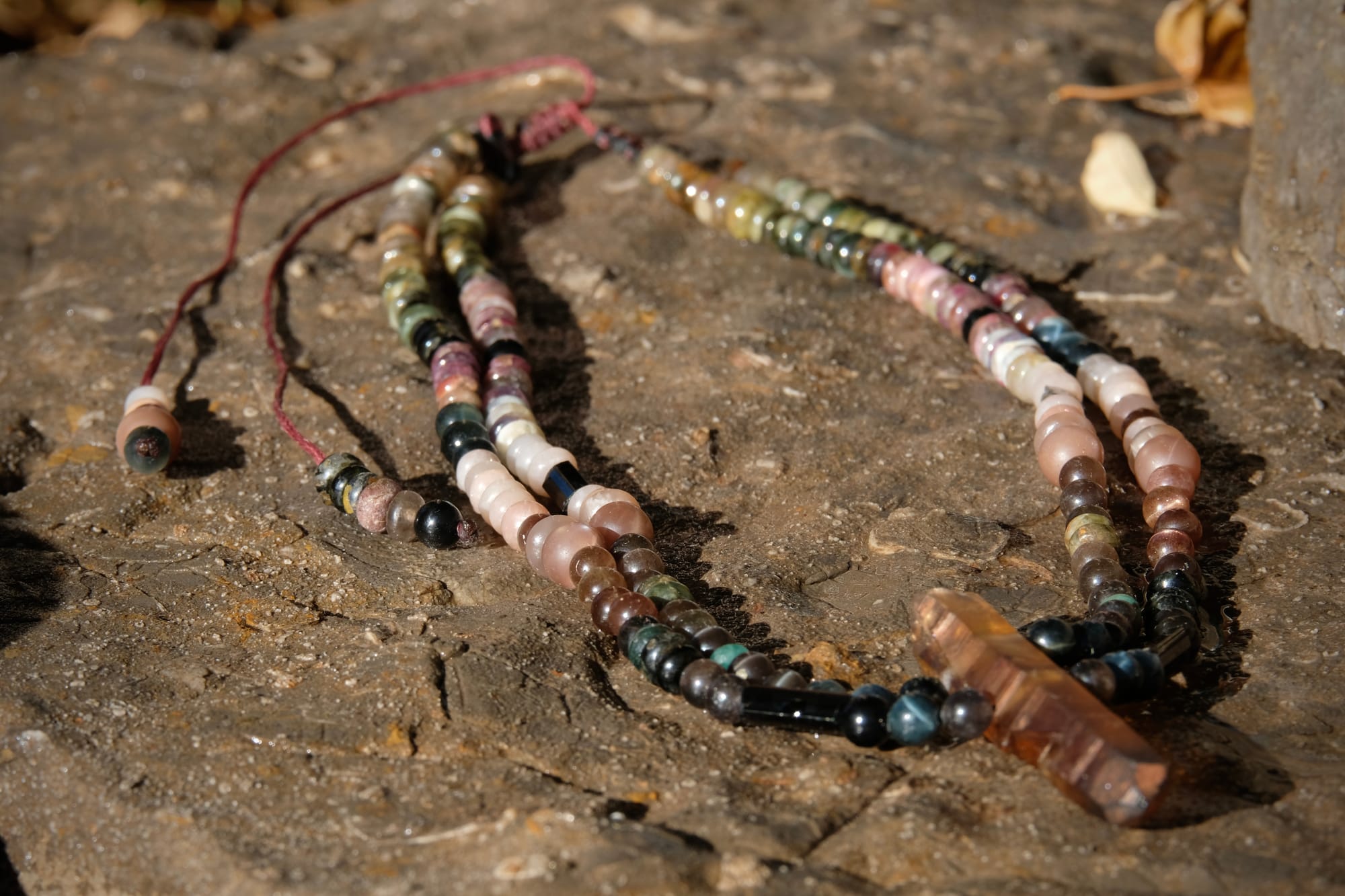 A citrine, cat's eye, tourmaline and emerald necklace by Jeannie Ortiza necklace of luminous semi precious stones in golden citrine, black, dusty pink and deep green rests on a stone embedded with fossils
