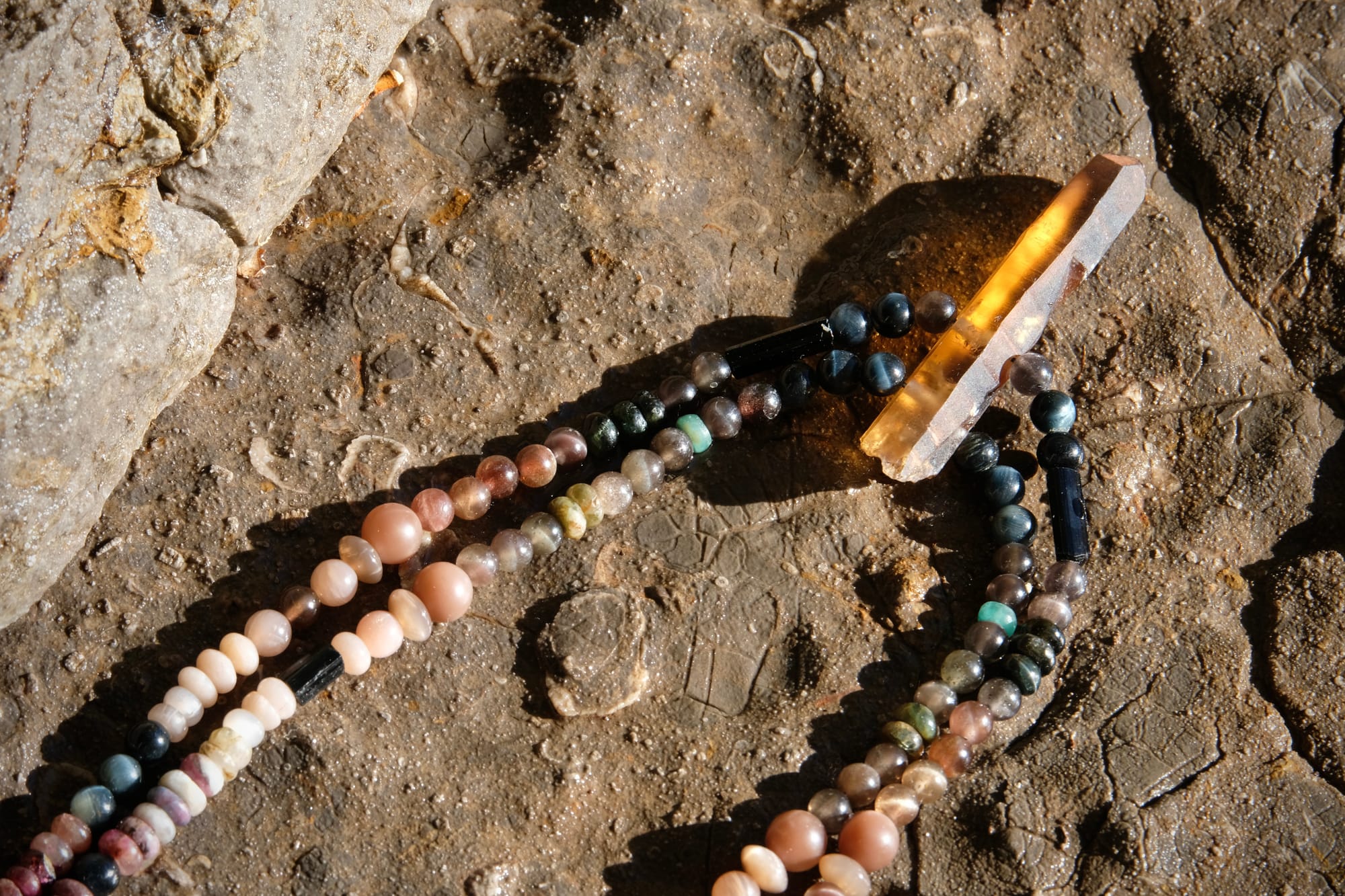 A citrine, cat's eye, tourmaline and emerald necklace by Jeannie Ortiza necklace of luminous semi precious stones in golden citrine, black, dusty pink and deep green rests on a stone embedded with fossils