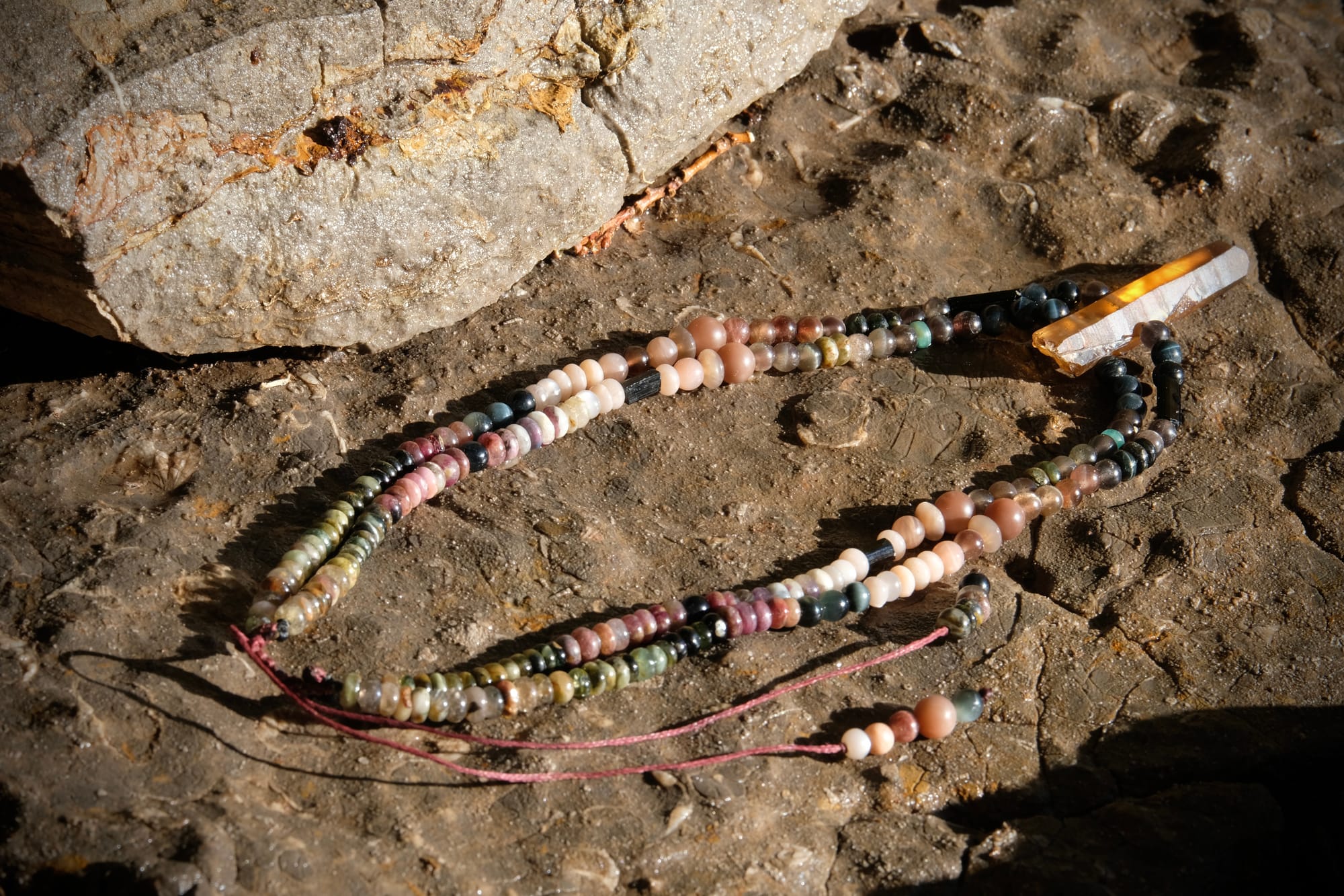 A citrine, cat's eye, tourmaline and emerald necklace by Jeannie Ortiza necklace of luminous semi precious stones in golden citrine, black, dusty pink and deep green rests on a stone embedded with fossils
