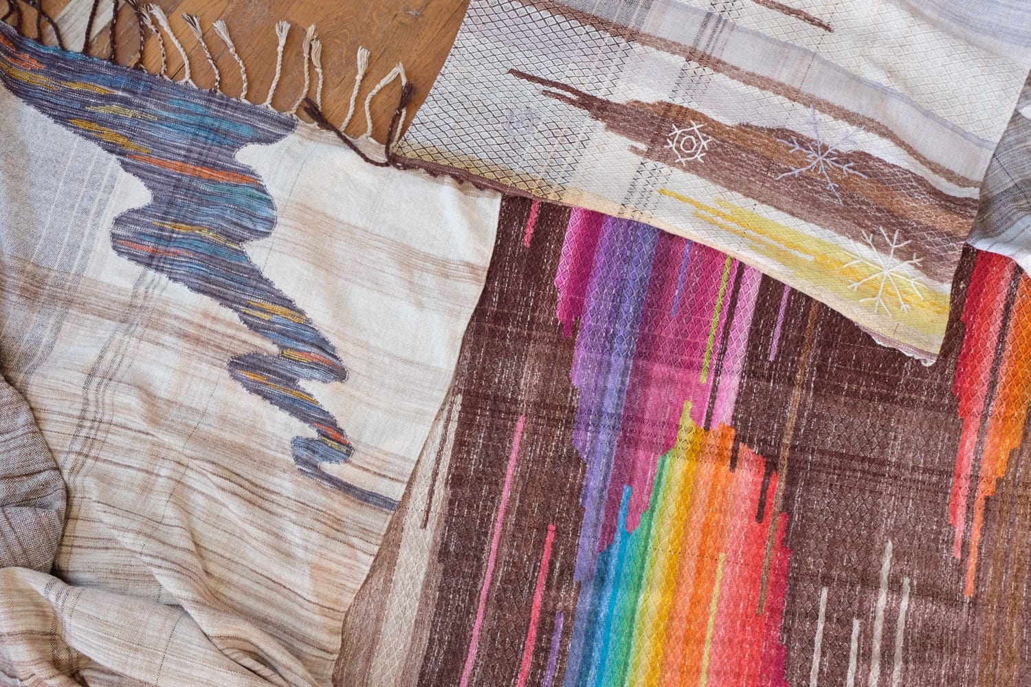 A length of handwoven fabric with details of fluid rainbows, a blue illuminated river and snowflakes