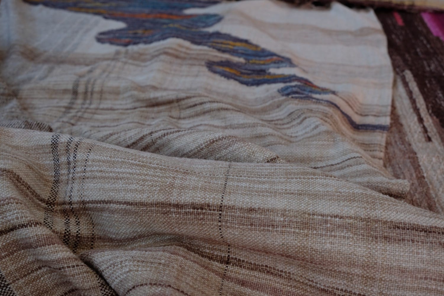 A length of handwoven fabric with details of fluid rainbows, a blue illuminated river and snowflakes