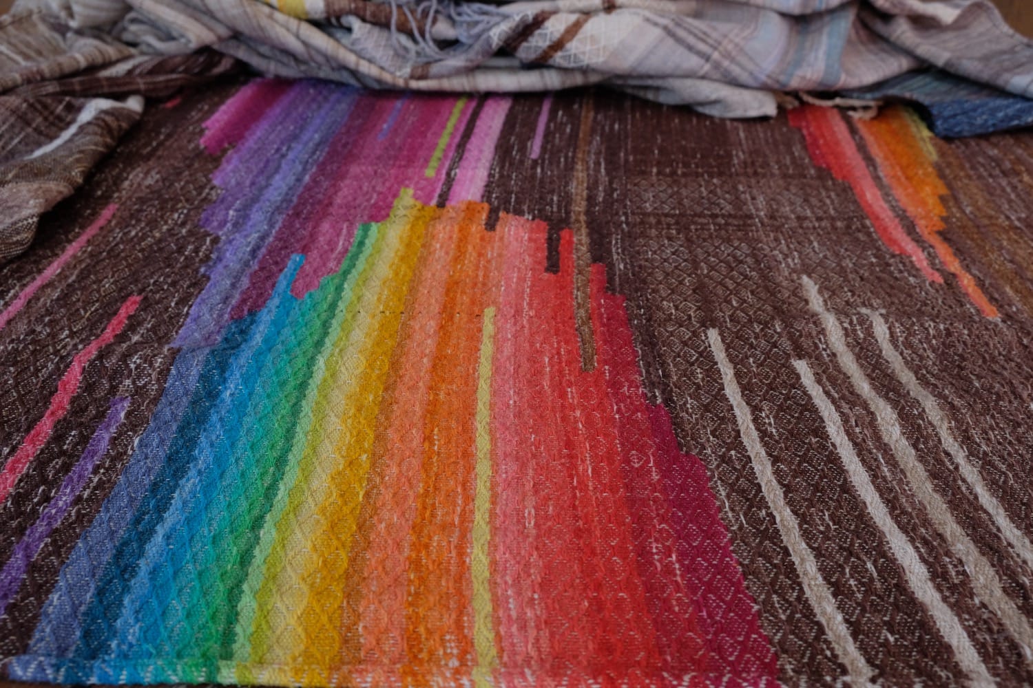 A length of handwoven fabric with details of fluid rainbows, a blue illuminated river and snowflakes