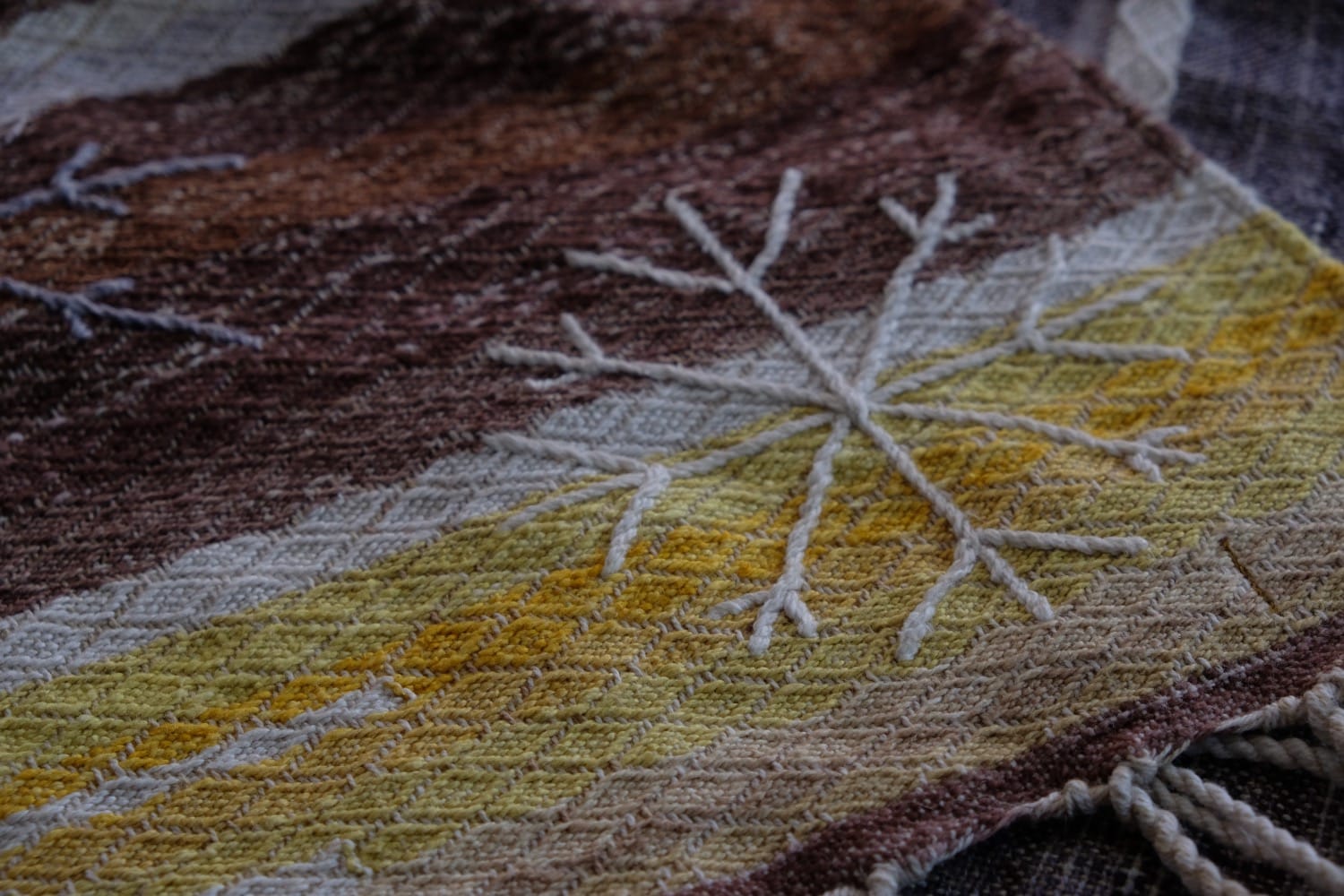 A length of handwoven fabric with details of fluid rainbows, a blue illuminated river and snowflakes