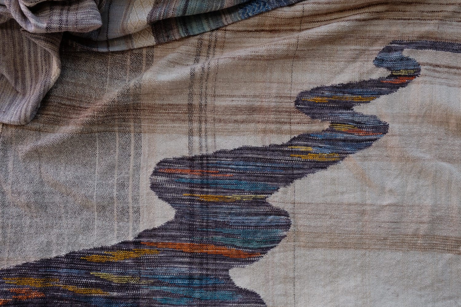 A length of handwoven fabric with details of fluid rainbows, a blue illuminated river and snowflakes