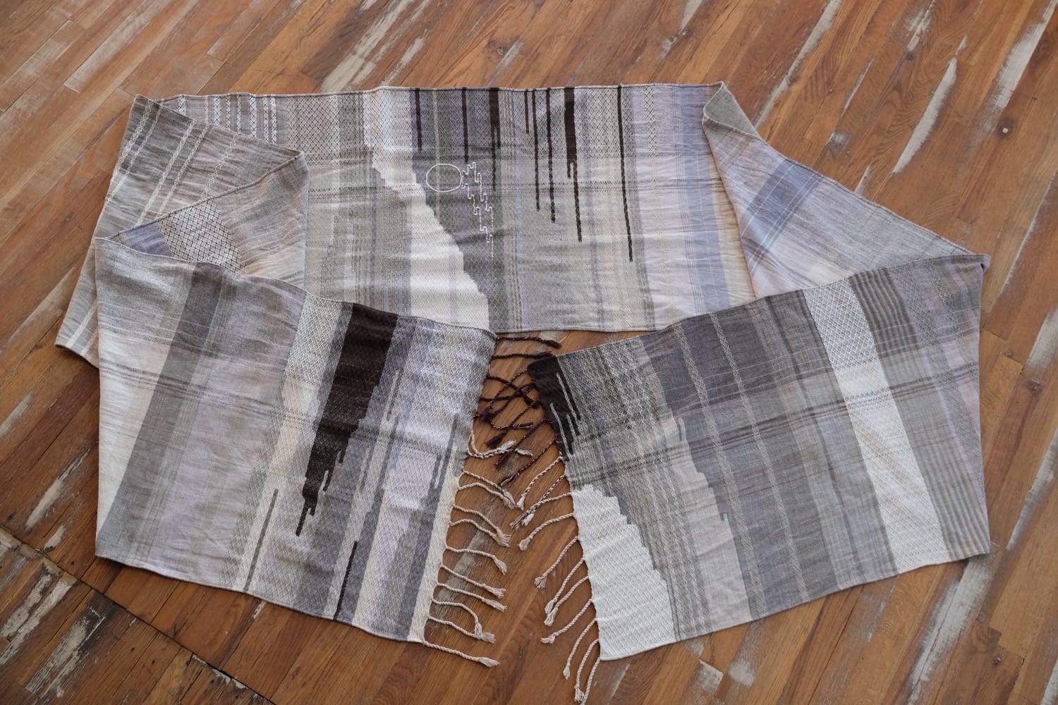 A detail of naturally dyed handwoven fabric in moody shades of gray, misty blue and black with a white moon in the middle