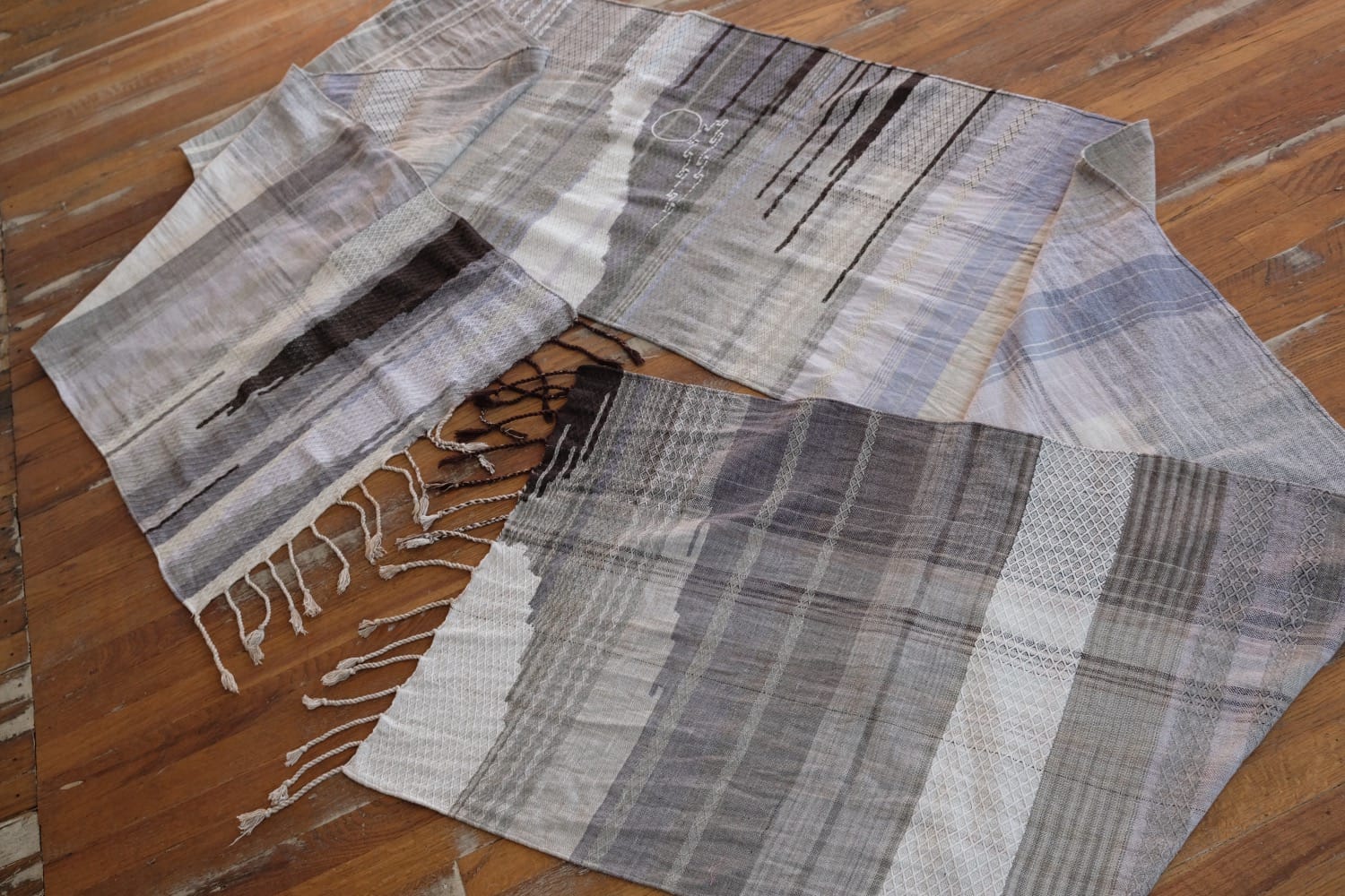 A detail of naturally dyed handwoven fabric in moody shades of gray, misty blue and black with a white moon in the middle and cloud designs throughout