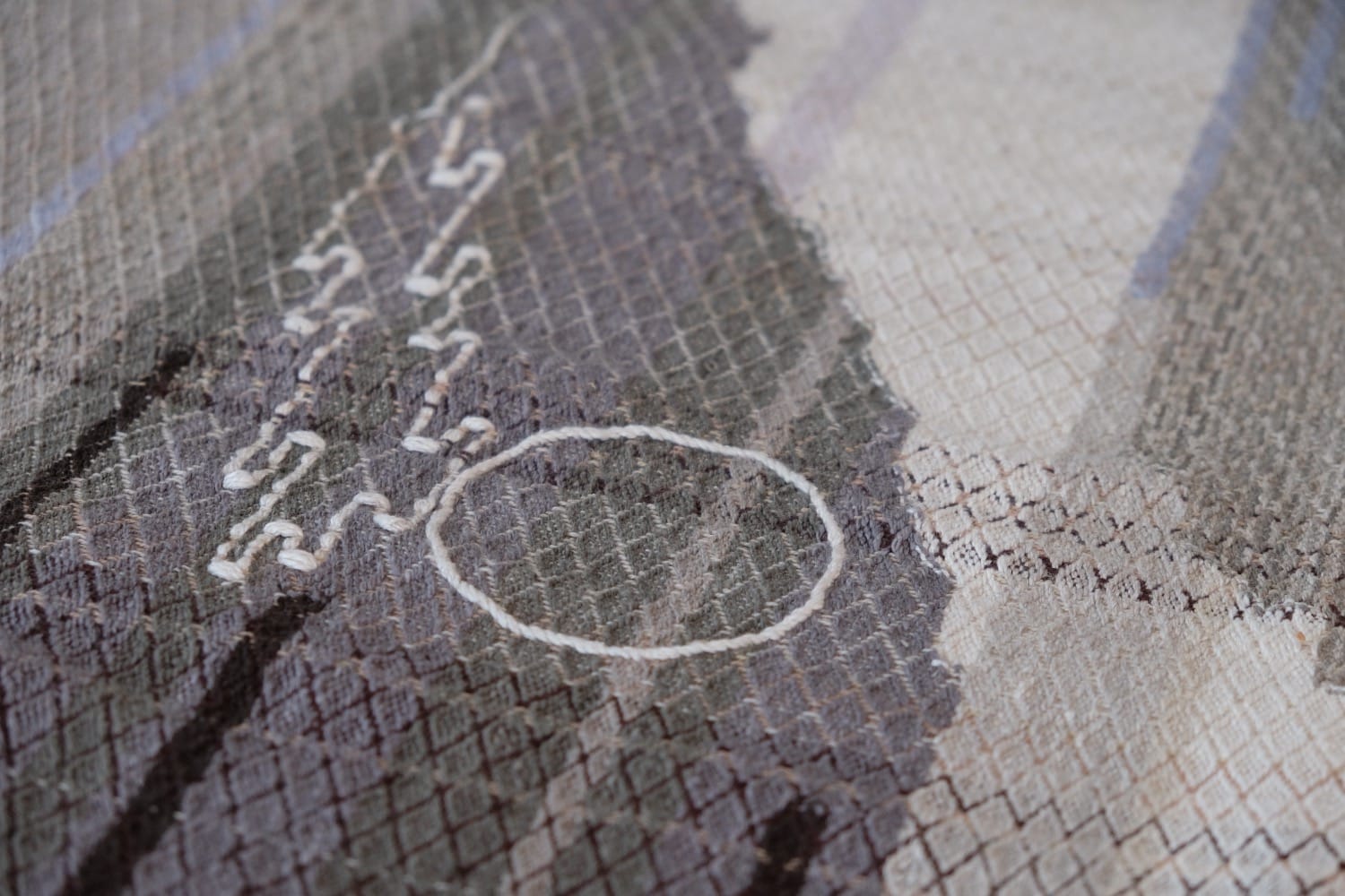 A detail of naturally dyed handwoven fabric in moody shades of gray, misty blue and black with a white moon in the middle