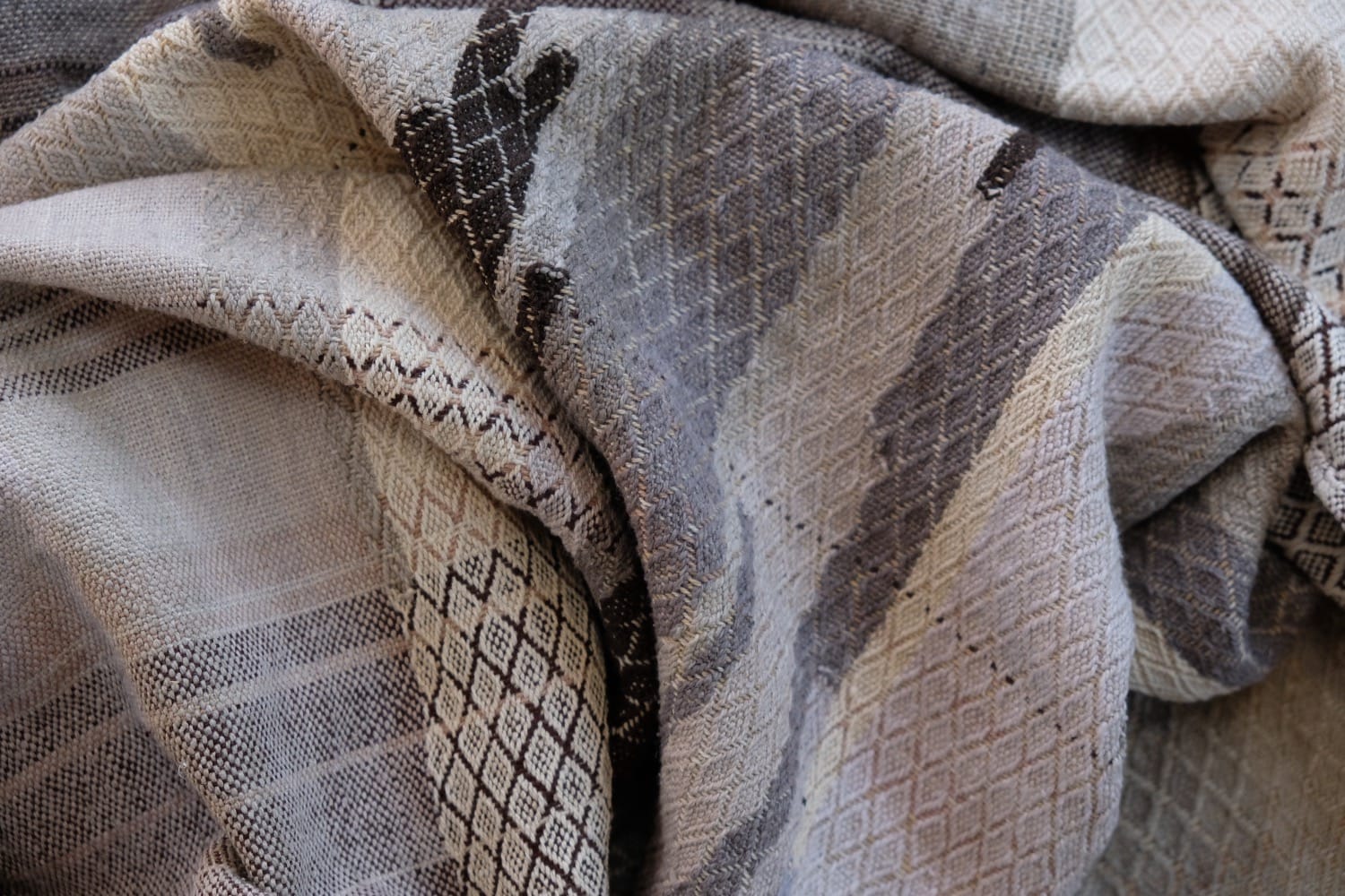 A detail of naturally dyed handwoven fabric in moody shades of gray, misty blue and black with a white moon in the middle and cloud designs throughout