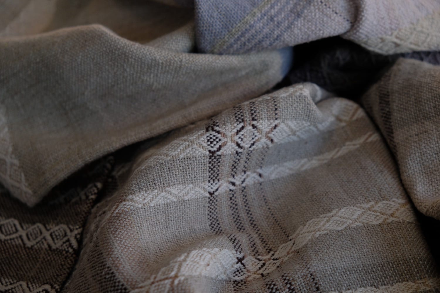 A detail of naturally dyed handwoven fabric in moody shades of gray, misty blue and black with a white moon in the middle and cloud designs throughout