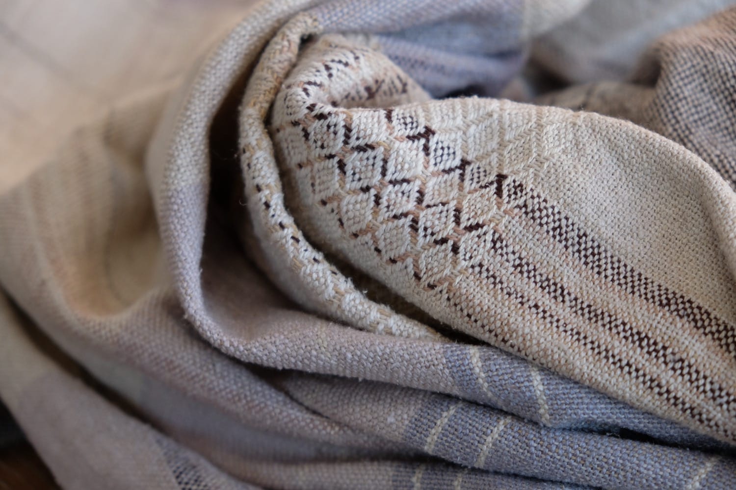 A detail of naturally dyed handwoven fabric in moody shades of gray, misty blue and black with a white moon in the middle and cloud designs throughout