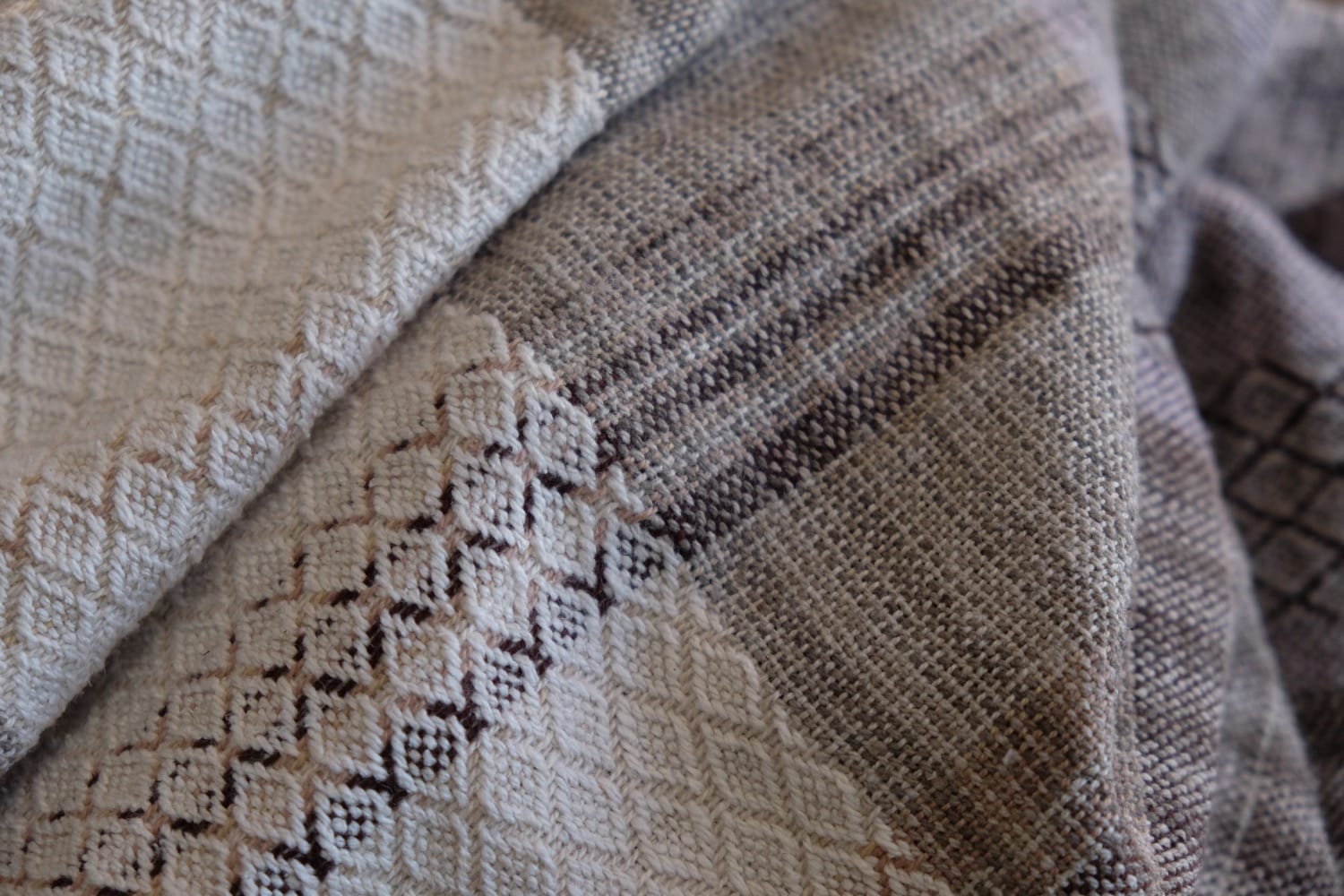A detail of naturally dyed handwoven fabric in moody shades of gray, misty blue and black with a white moon in the middle and cloud designs throughout