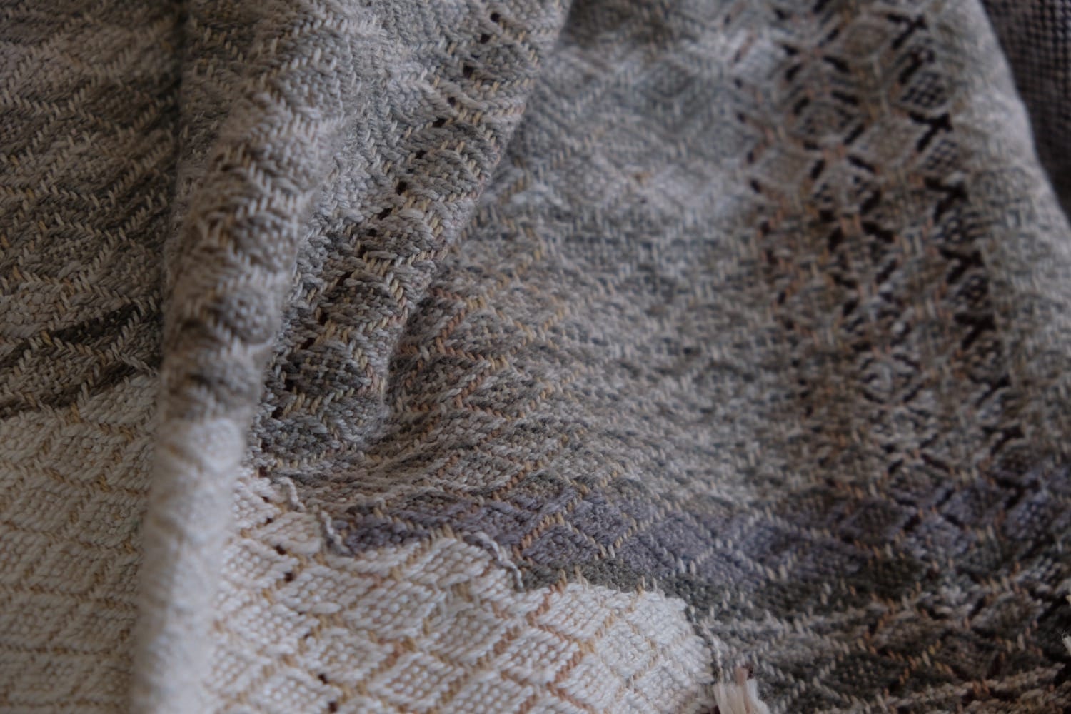 A detail of naturally dyed handwoven fabric in moody shades of gray, misty blue and black with a white moon in the middle and cloud designs throughout