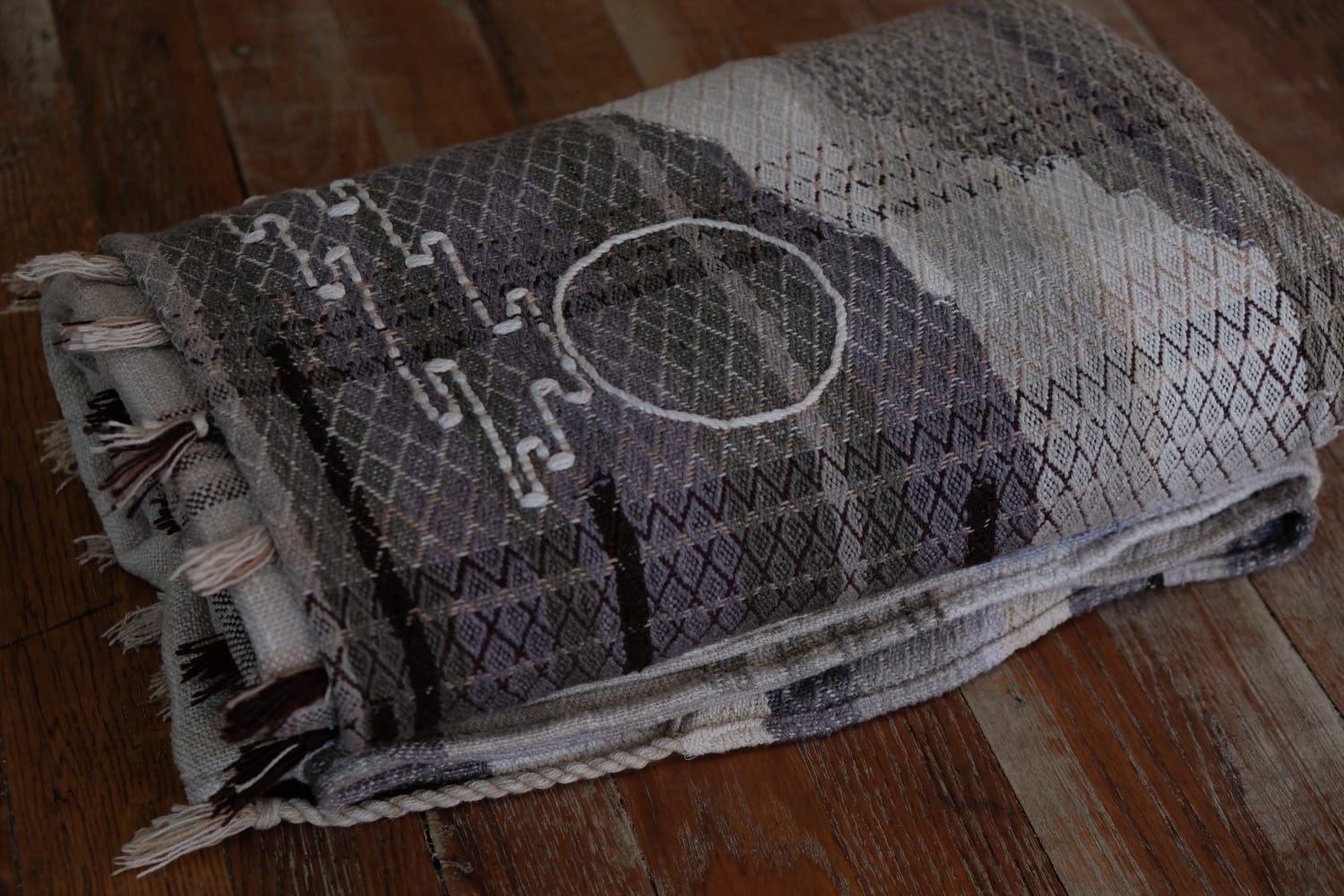 A detail of naturally dyed handwoven fabric in moody shades of gray, misty blue and black with a white moon in the middle and cloud designs throughout