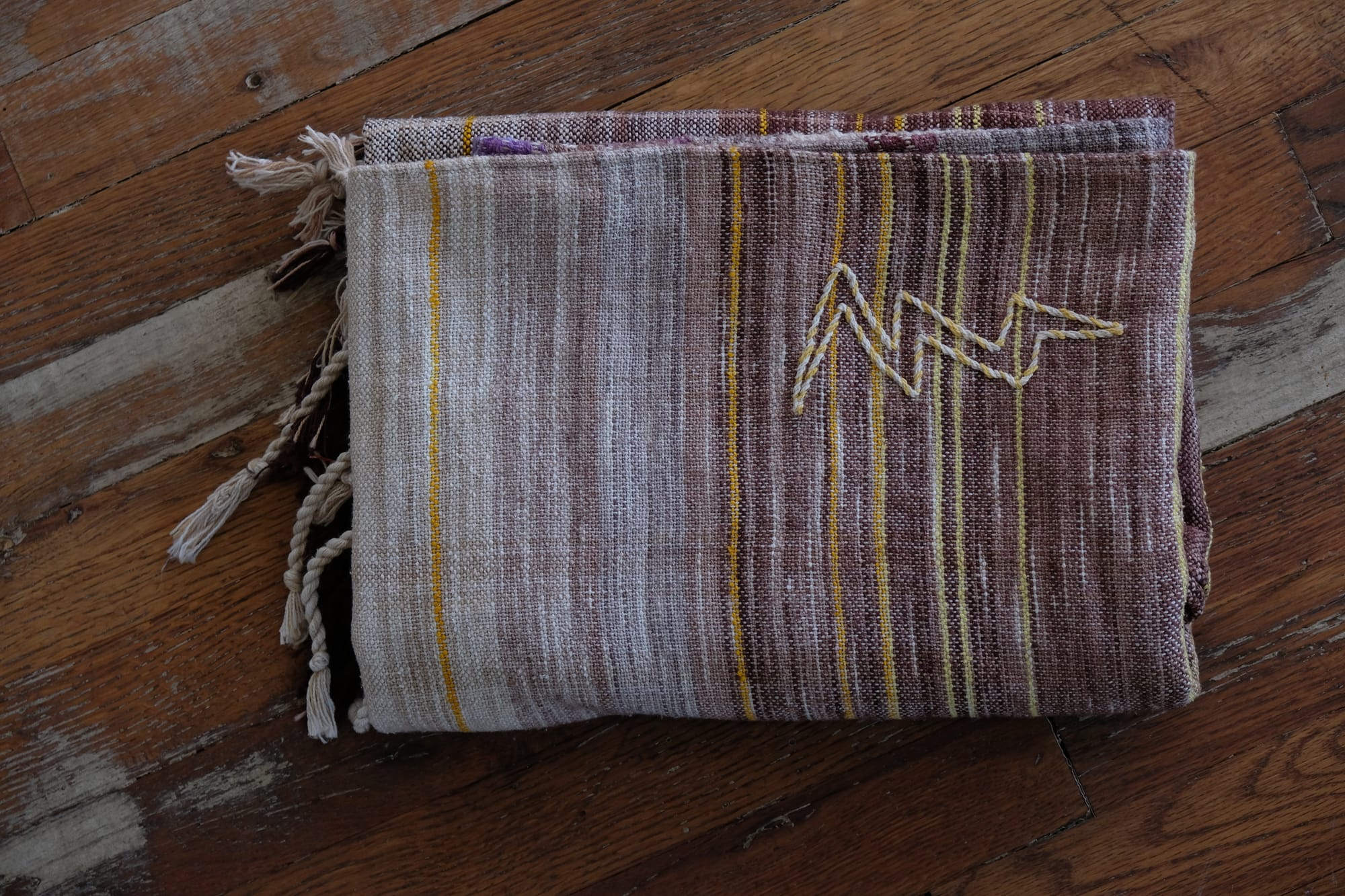A handwoven shawl with hand dyed raw silk in grey, brown, yellow, purple and red with a lightning bolt detail