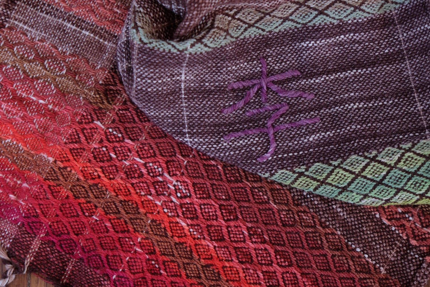A handwoven shawl with hand dyed raw silk in grey, brown, yellow, purple and red with a Chinese character for plum woven detail