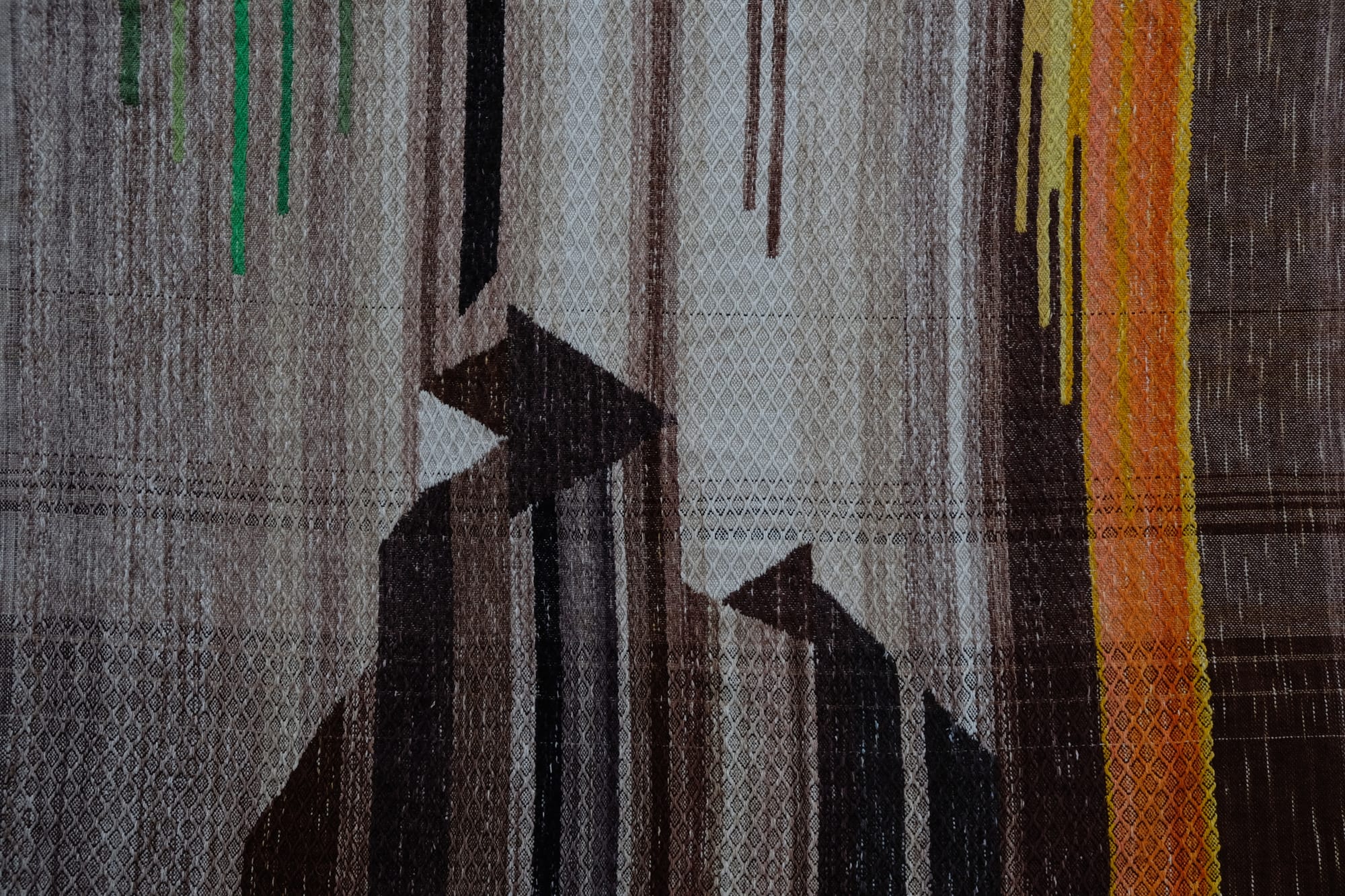 A detail of the geometric tapestry woven designs on a shawl in grayscale, earth-tones and elemental colors of lavender, orange poppy, water and grass. The shawl is laying on a wooden floor