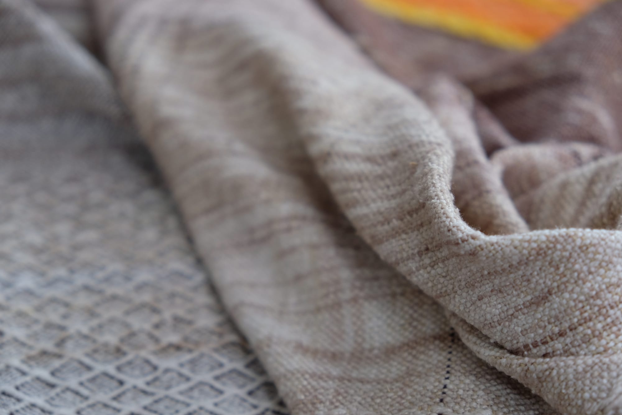 A detail of the geometric tapestry woven designs on a shawl in grayscale, earth-tones and elemental colors of lavender, orange poppy, water and grass. The shawl is laying on a wooden floor