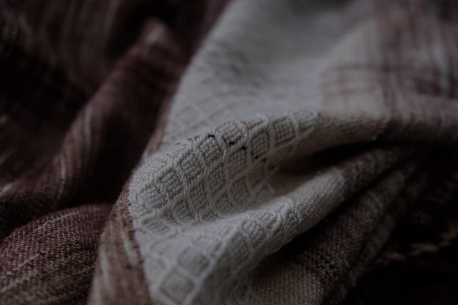 A detail of a length of handwoven fabric in earth-tones and all the colors of the rainbow in prismatic sequence, laid out on a wood floor