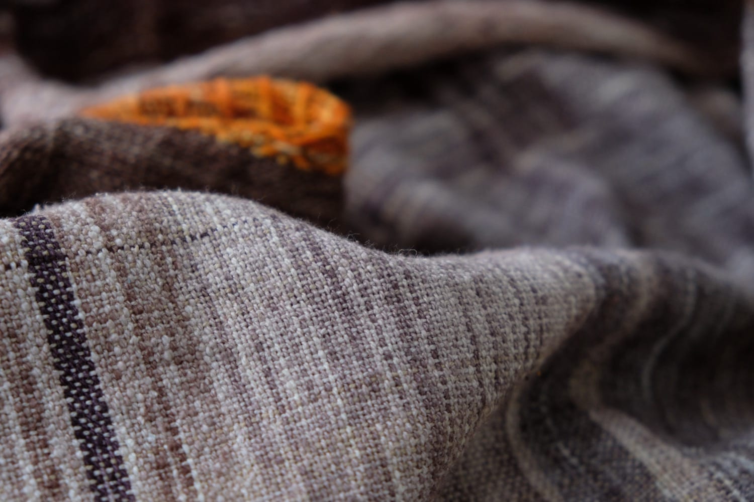 A detail of a length of handwoven fabric in earth-tones and all the colors of the rainbow in prismatic sequence, laid out on a wood floor