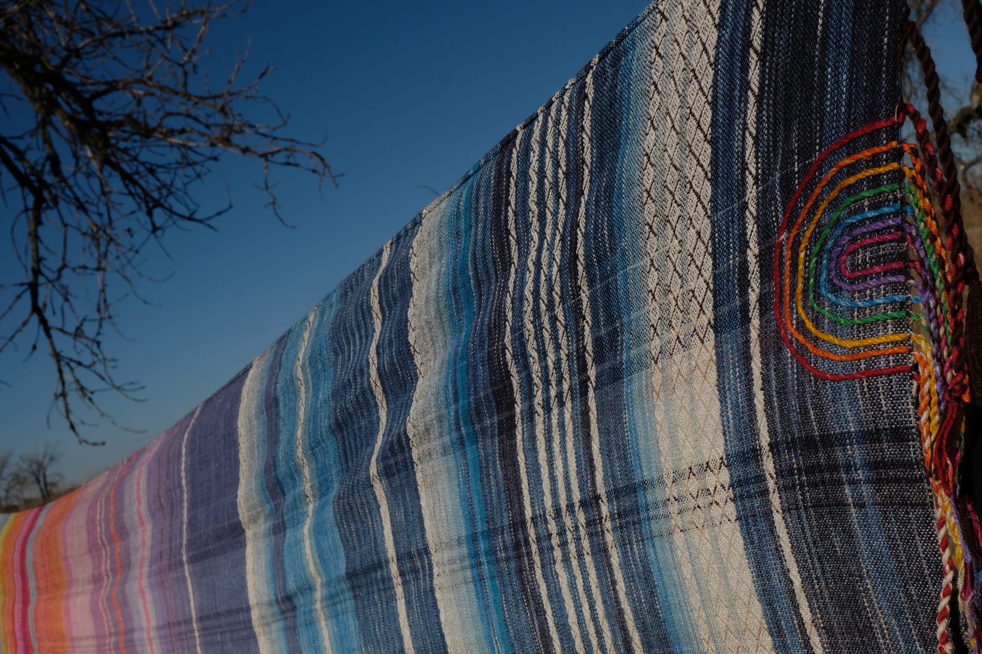 a long length of handwoven fabric in the colors of blue sky, sunrise and dry fields of barley