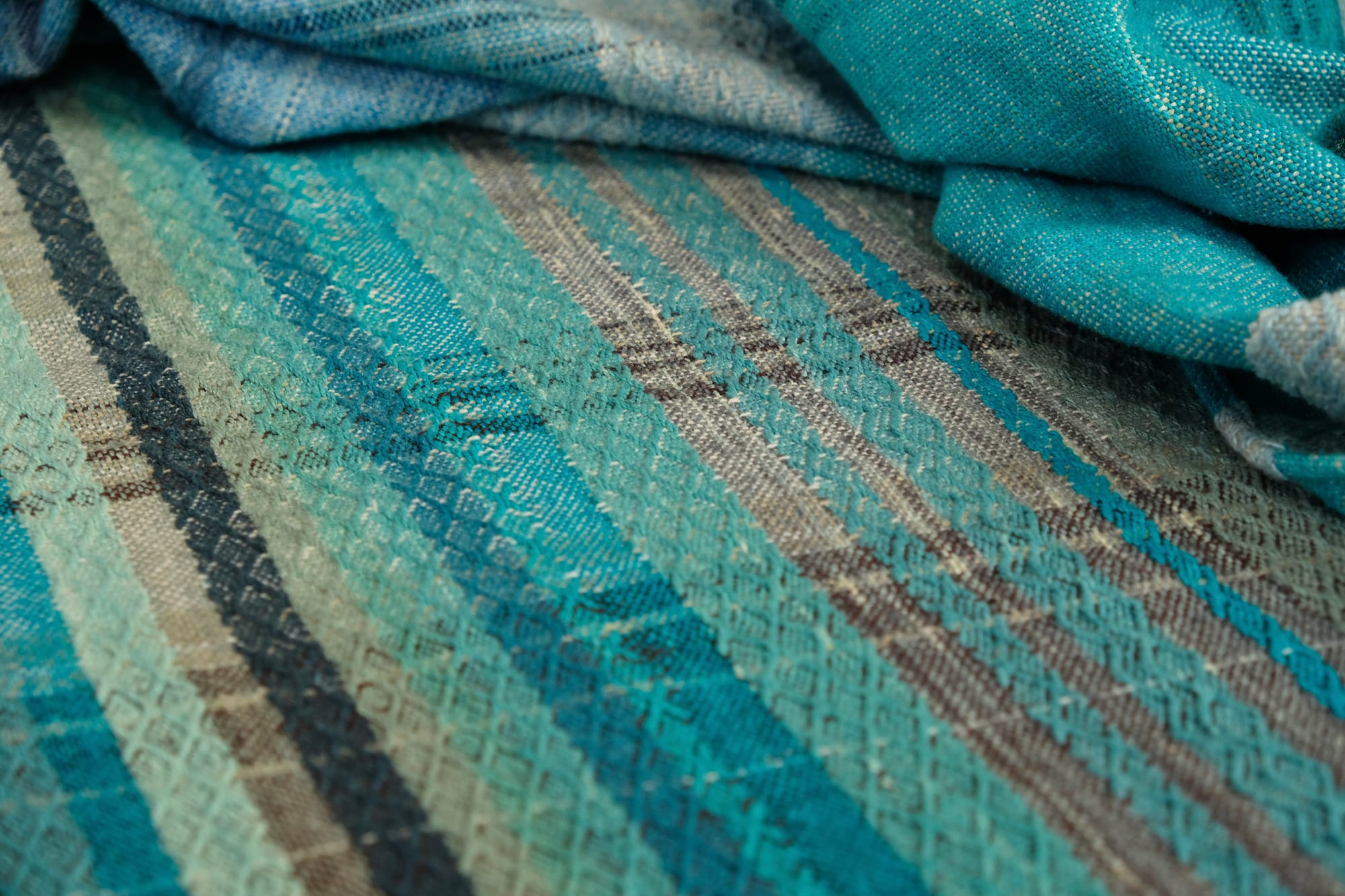 on an oak wood floor is laid 5 meters of handwoven fabric in textured stripes of greens on one side and shades of blue on the other
