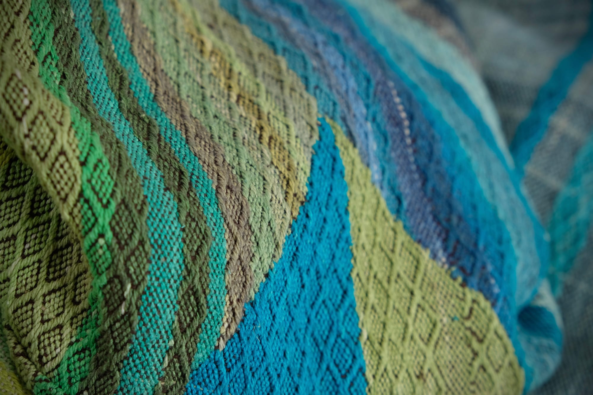 on an oak wood floor is laid 5 meters of handwoven fabric in textured stripes of greens on one side and shades of blue on the other