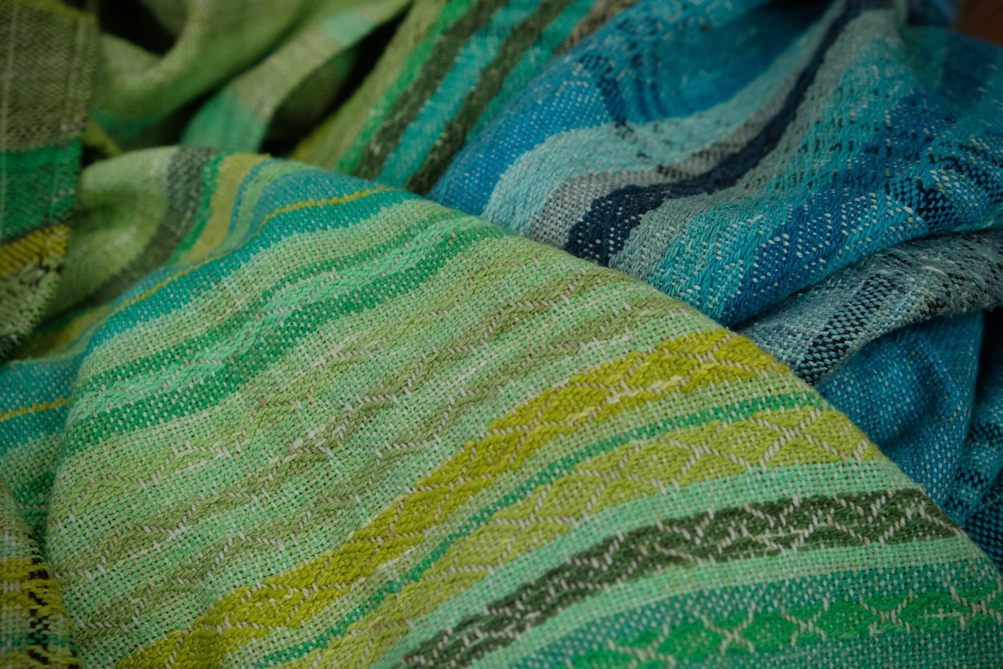 on an oak wood floor is laid 5 meters of handwoven fabric in textured stripes of greens on one side and shades of blue on the other