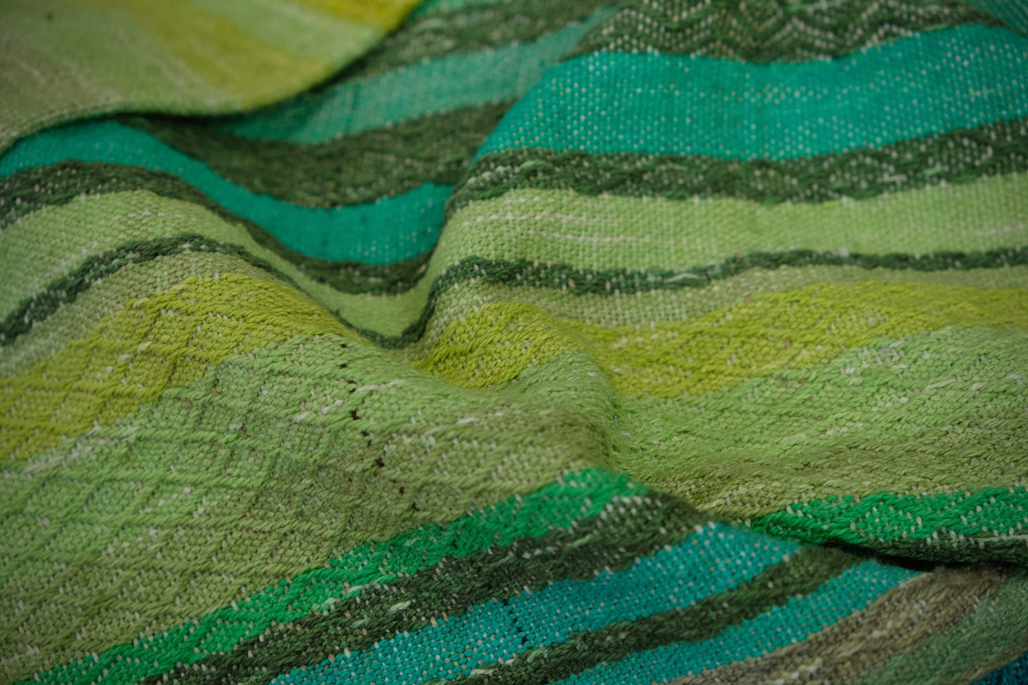 on an oak wood floor is laid 5 meters of handwoven fabric in textured stripes of greens on one side and shades of blue on the other