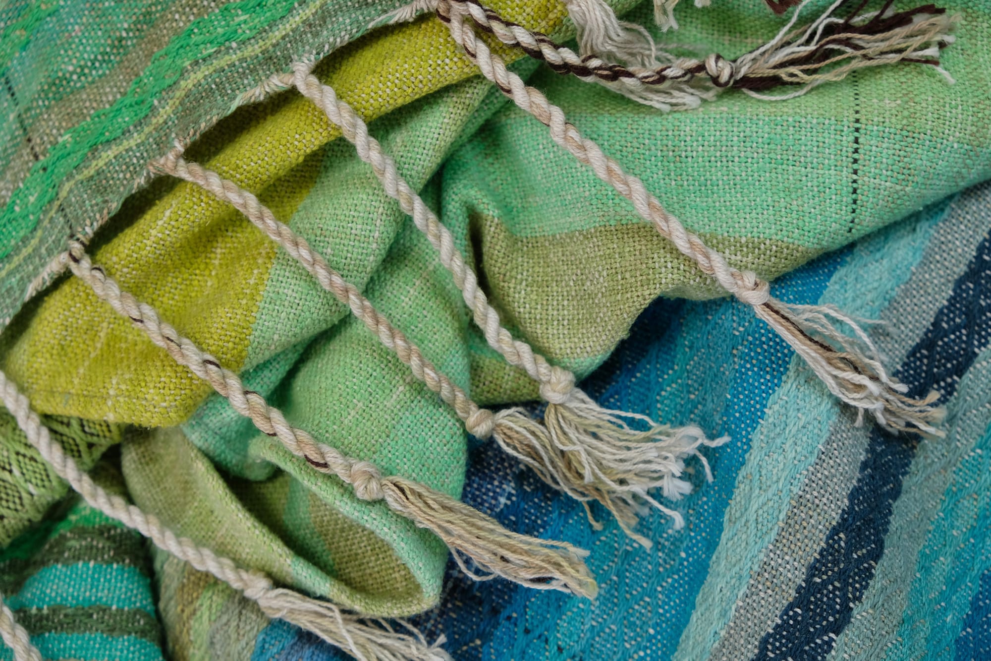 a detail of the fringe on the end of on an oak wood floor is laid 5 meters of handwoven fabric in textured stripes of greens on one side and shades of blue on the other