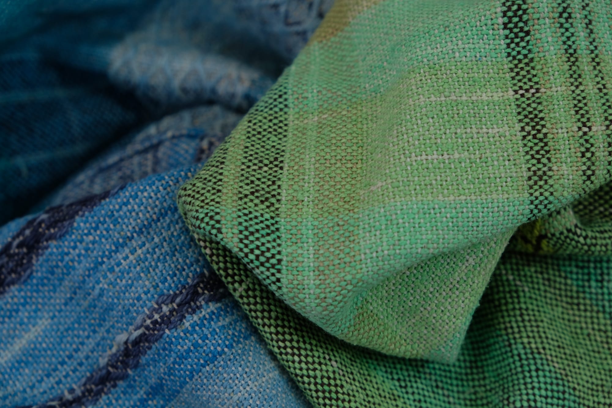 a detail of on an oak wood floor is laid 5 meters of handwoven fabric in textured stripes of greens on one side and shades of blue on the other