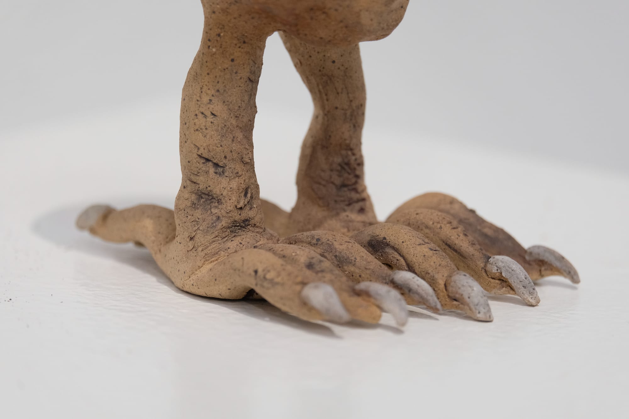 A small clay sculpture of a human head with raven legs. The clay is tan with dark speckles, the toenails of the creature are painted white