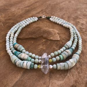green-blue amazonite necklace with a double terminated quartz point laying on a flat, tan stone